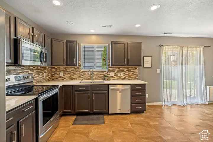 Kitchen featuring dark wood-finish cabinetry, stainless steel appliances, a mosaic tile backsplash, and light-toned countertops