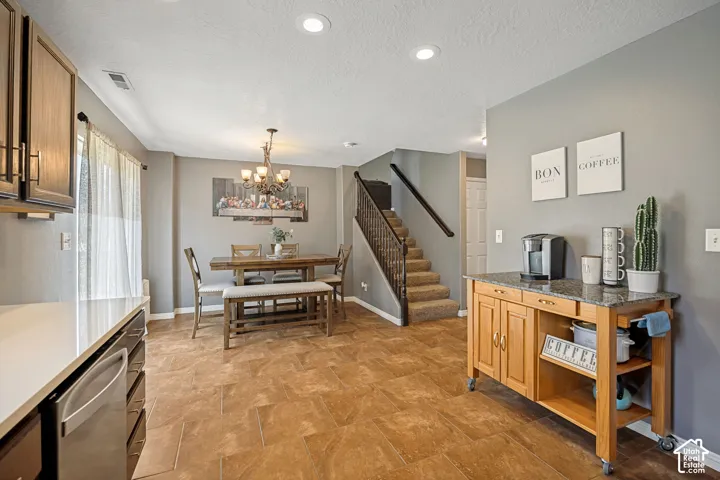 Kitchen and dining area featuring recessed lighting, a stainless steel dishwasher, wood-finish cabinetry, and a dining table with a bench and chairs under a chandelier