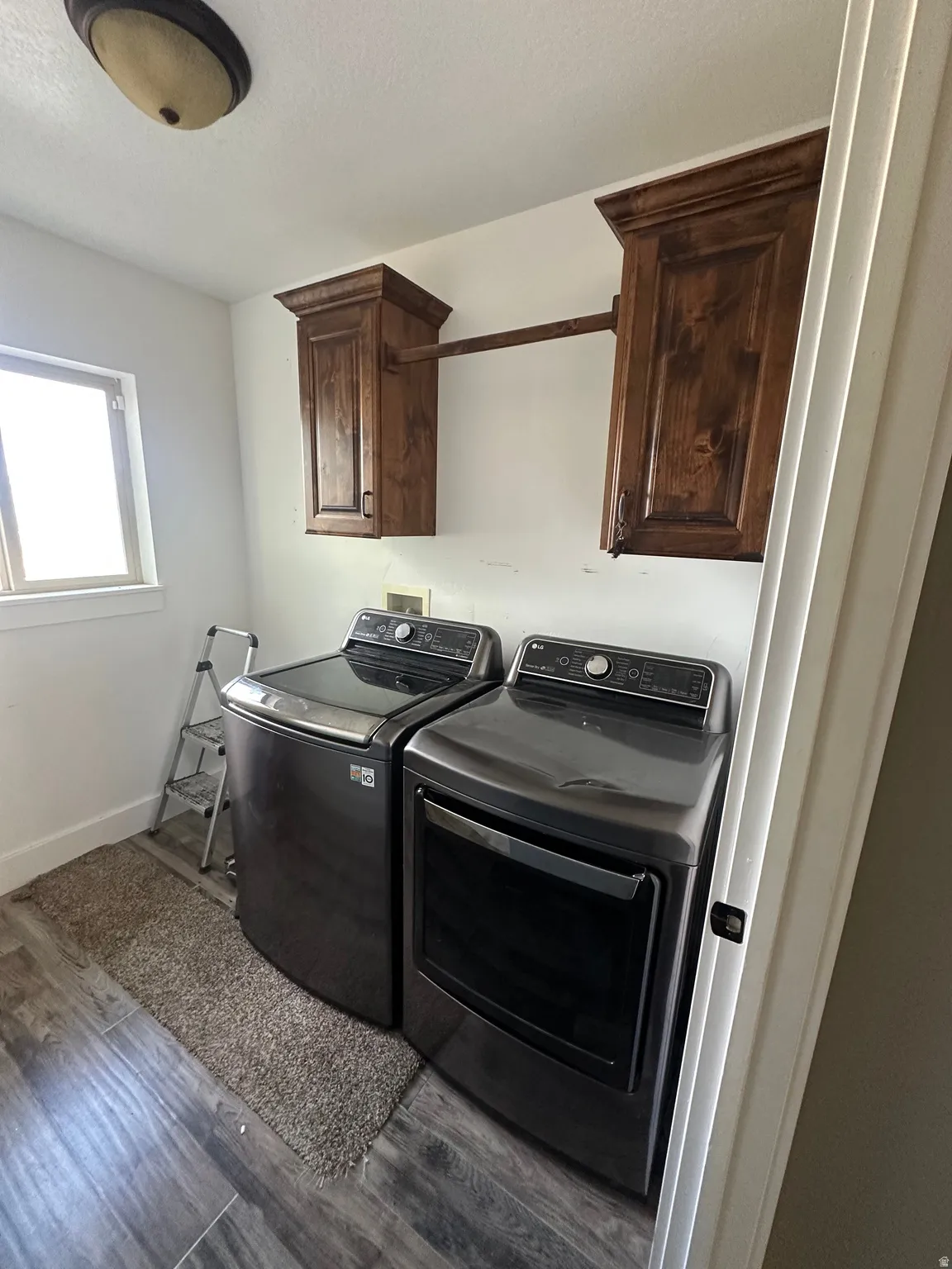 Laundry room featuring wood-finish flooring, a window providing natural light, and overhead wood cabinetry with a clothes rod