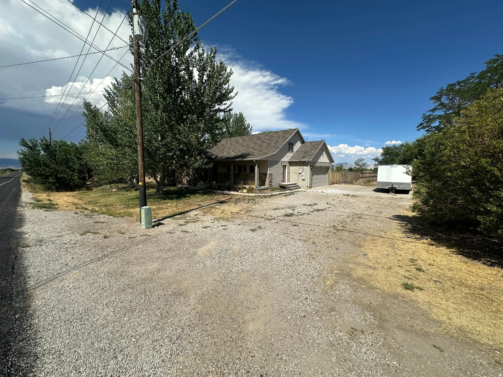 Gravel driveway with ample parking, mature trees, and a two-car attached garage
