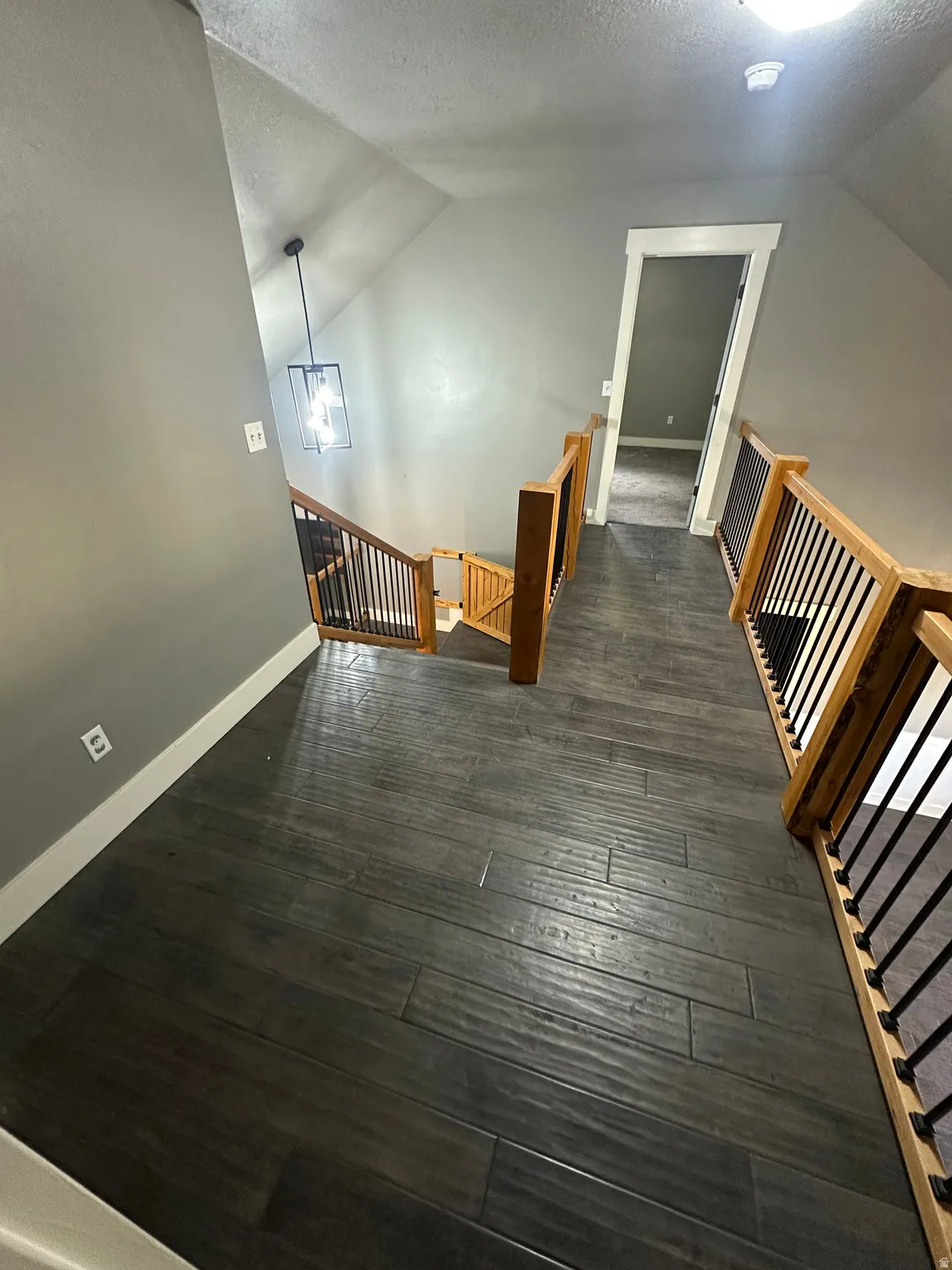 Upper-level hallway featuring dark wood-finish flooring, light-toned walls, and a modern geometric pendant light fixture