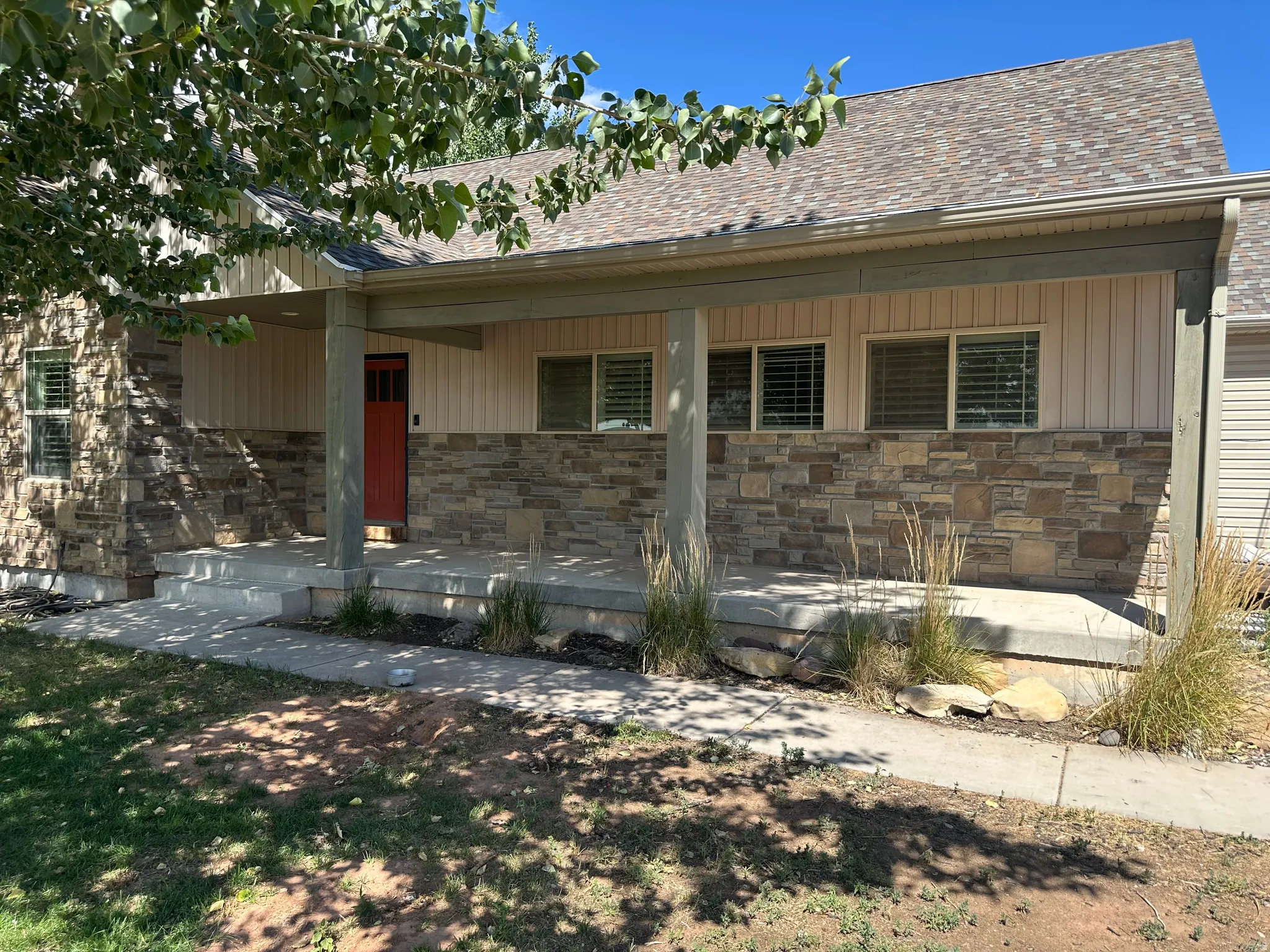 Covered front porch featuring stacked stone accents, vertical panel siding, and a red entry door
