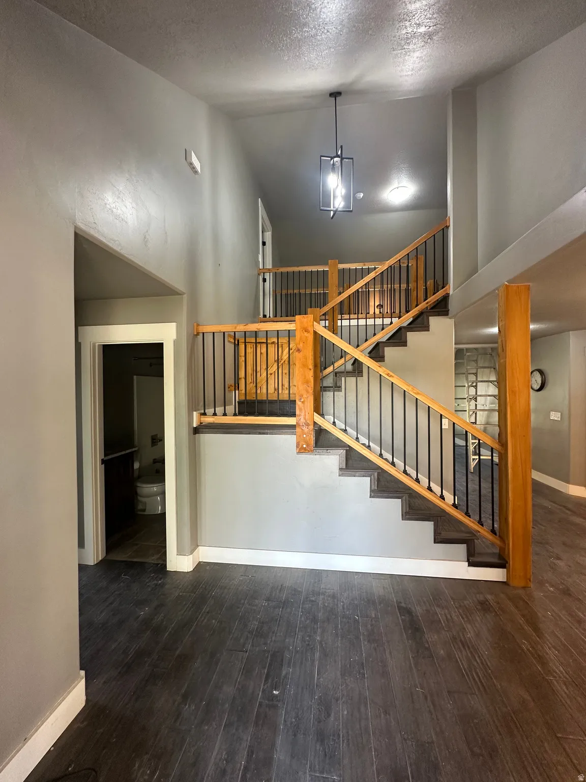 Two-story entry featuring dark wood-finish flooring, a contemporary black lantern pendant light, and a staircase with natural wood railings and black metal balusters