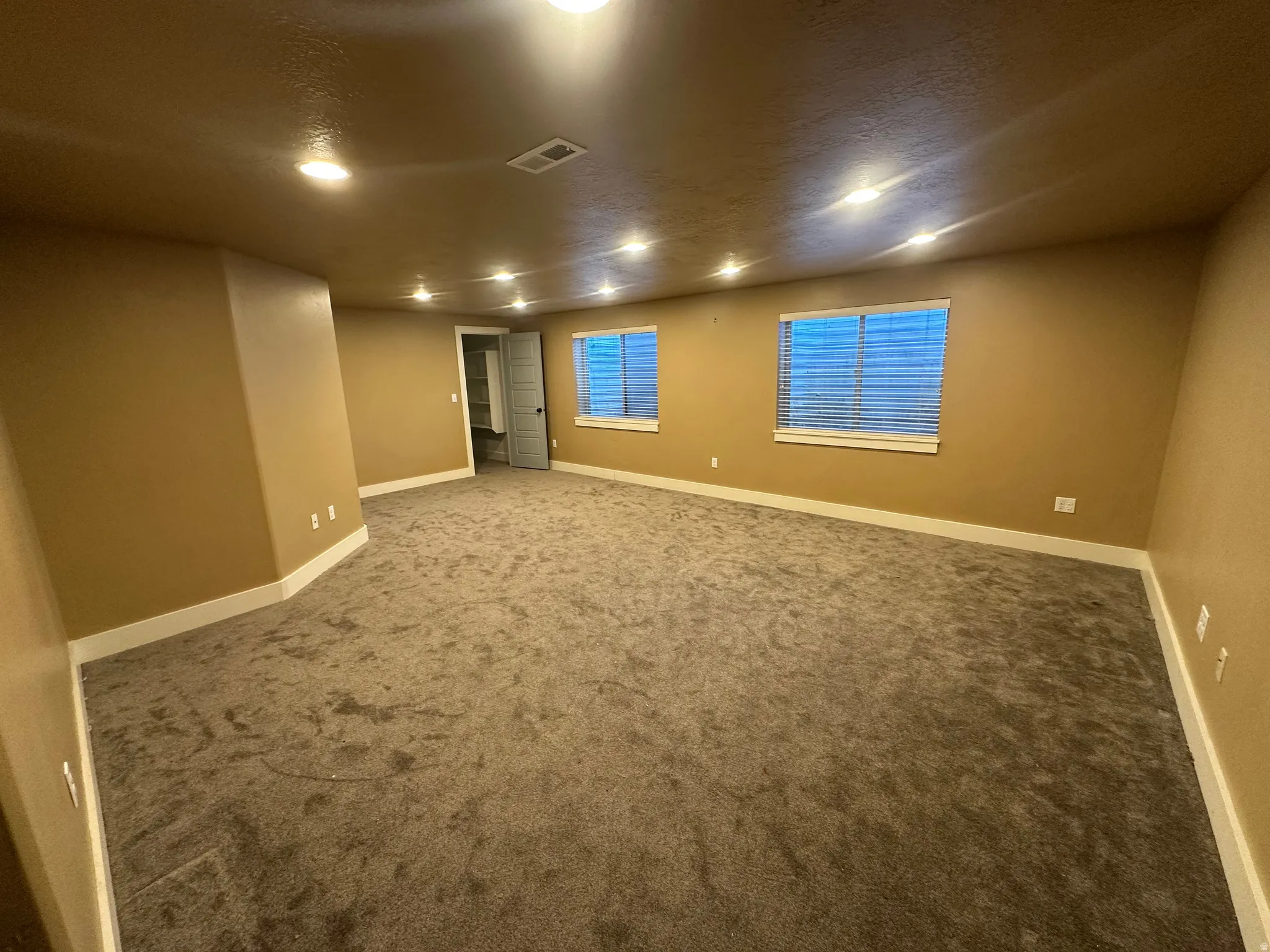 Spacious room featuring plush carpet, multiple windows with blinds, recessed lighting, and crisp white baseboards