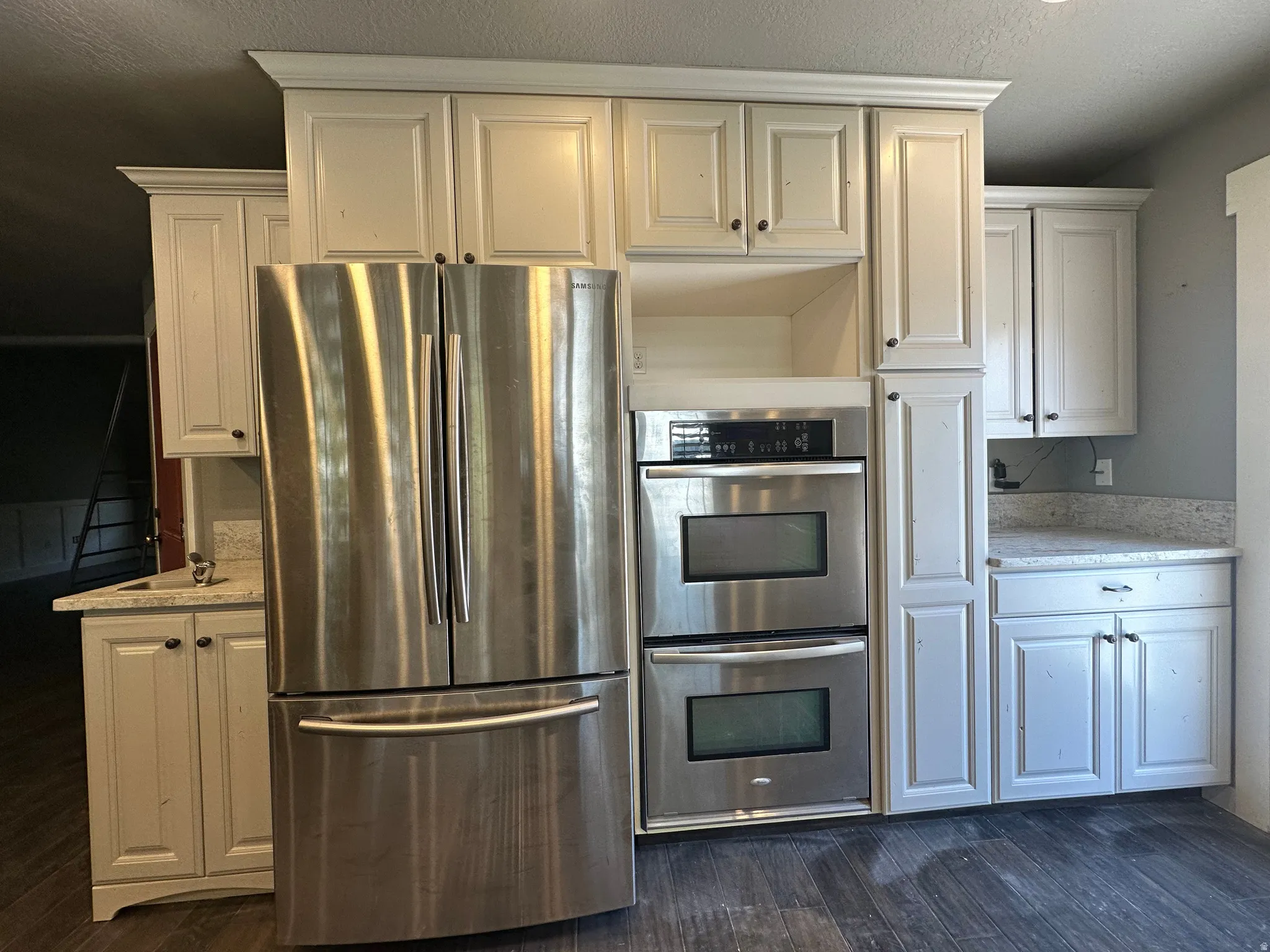 Kitchen featuring stainless steel appliances, stacked ovens, shaker-style cabinetry, light-toned countertops, and wood-finish flooring