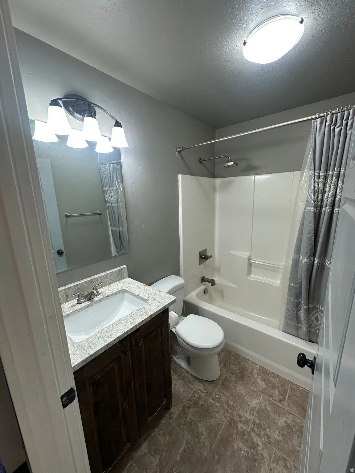 Bathroom featuring a wood-finish vanity with a light-toned countertop, an integrated sink, a full bathtub with a shower, and tiled flooring