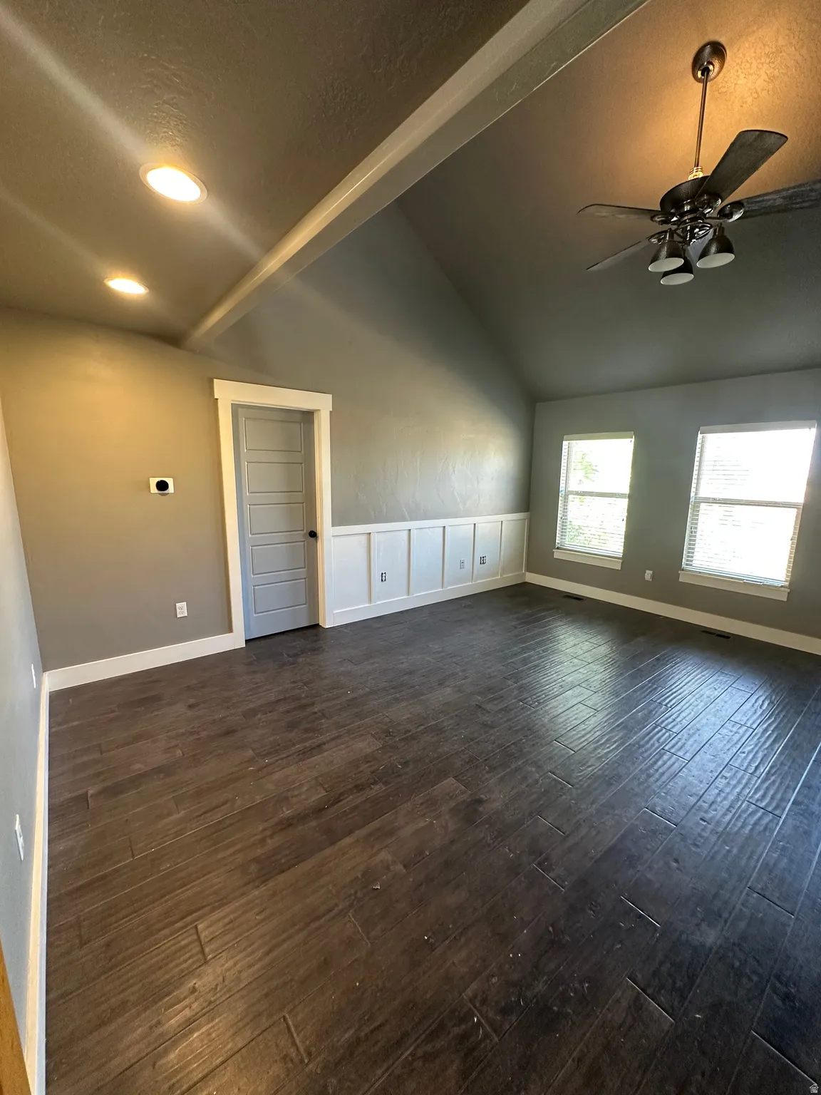 Spacious room featuring vaulted ceilings, wood-finish flooring, a contemporary ceiling fan, recessed lighting, and wainscoting detailing
