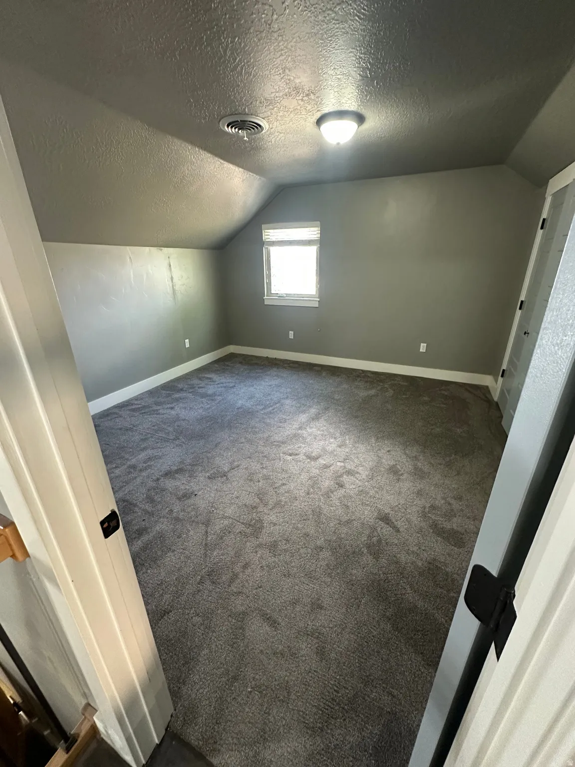 Spacious room featuring vaulted ceilings, a single window with blinds, and gray plush carpeting