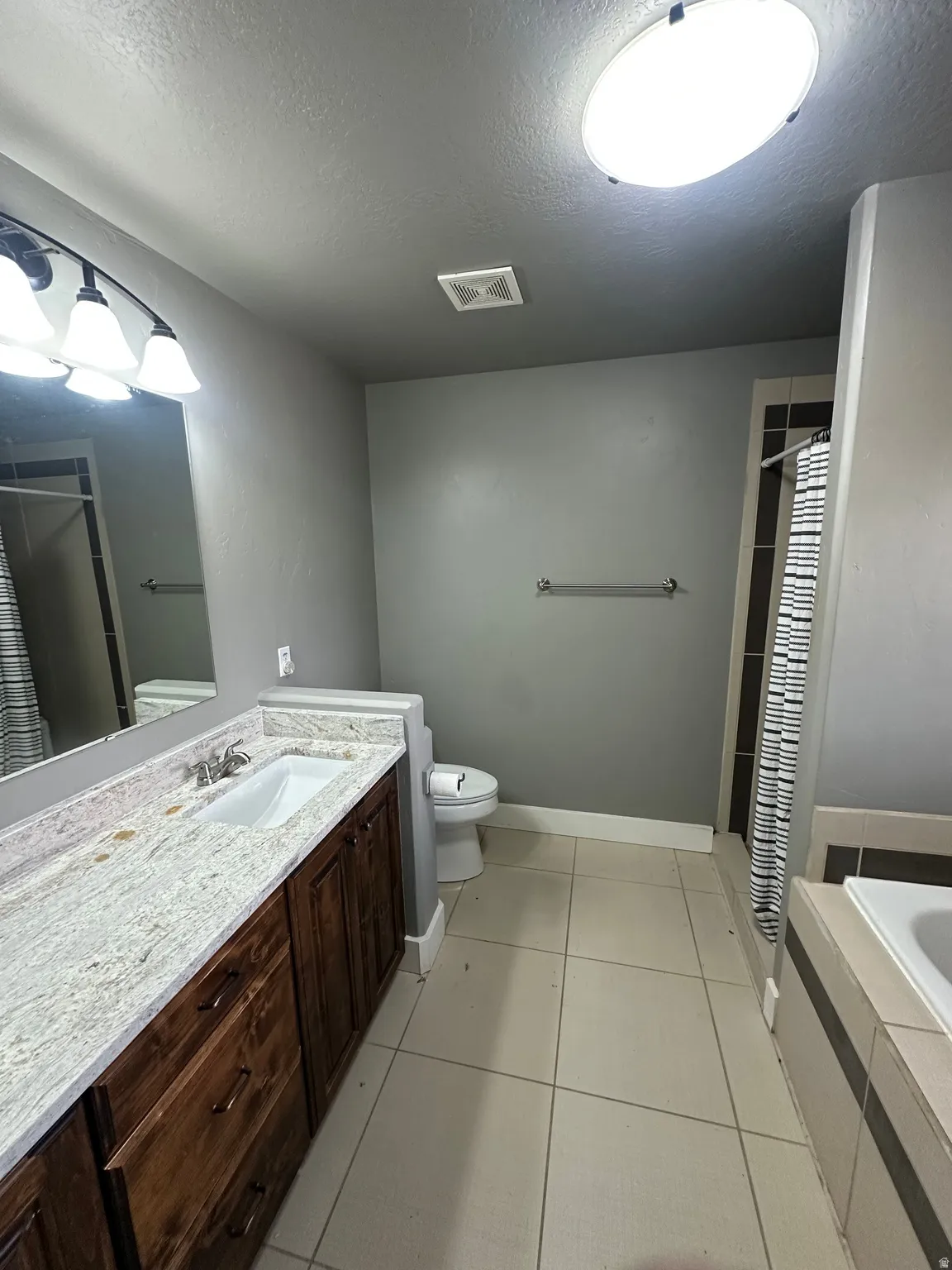 Bathroom featuring a dual-sink vanity with a granite countertop, ceramic tile flooring, a built-in tub, and an overhead lighting fixture
