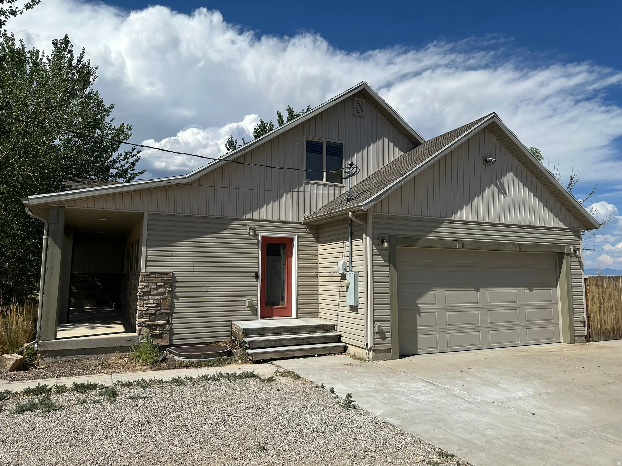 Exterior featuring horizontal siding with vertical siding accents, a red entry door, an attached garage, and stone veneer detailing
