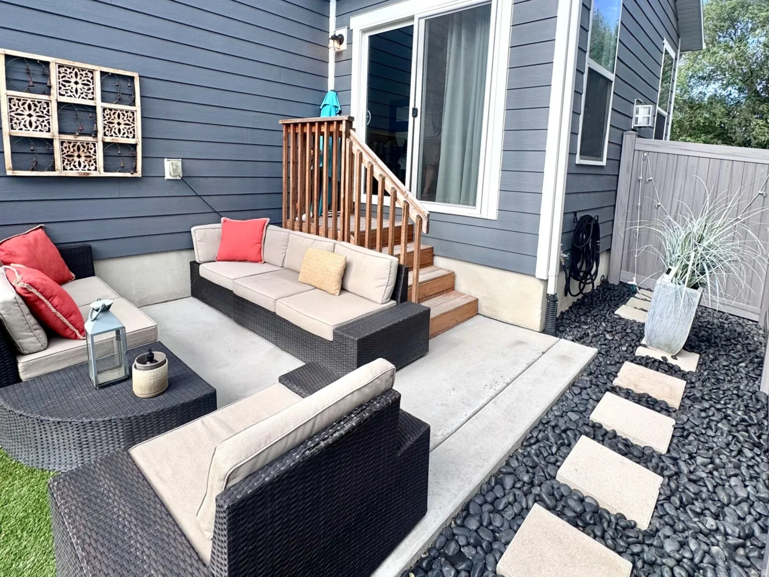 Concrete patio with built-in seating, dark siding, sliding glass door, wooden steps, and a decorative pebble pathway