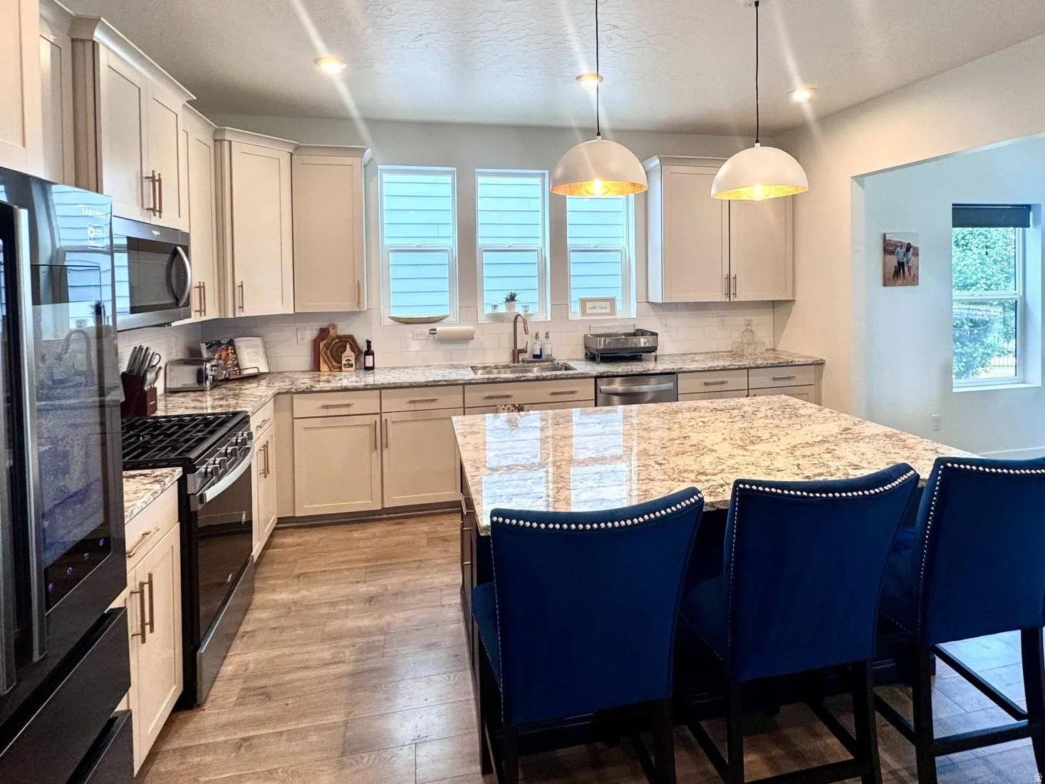 Modern kitchen featuring a large central island with a light-toned countertop, wood-finish flooring, recessed lighting, and pendant fixtures