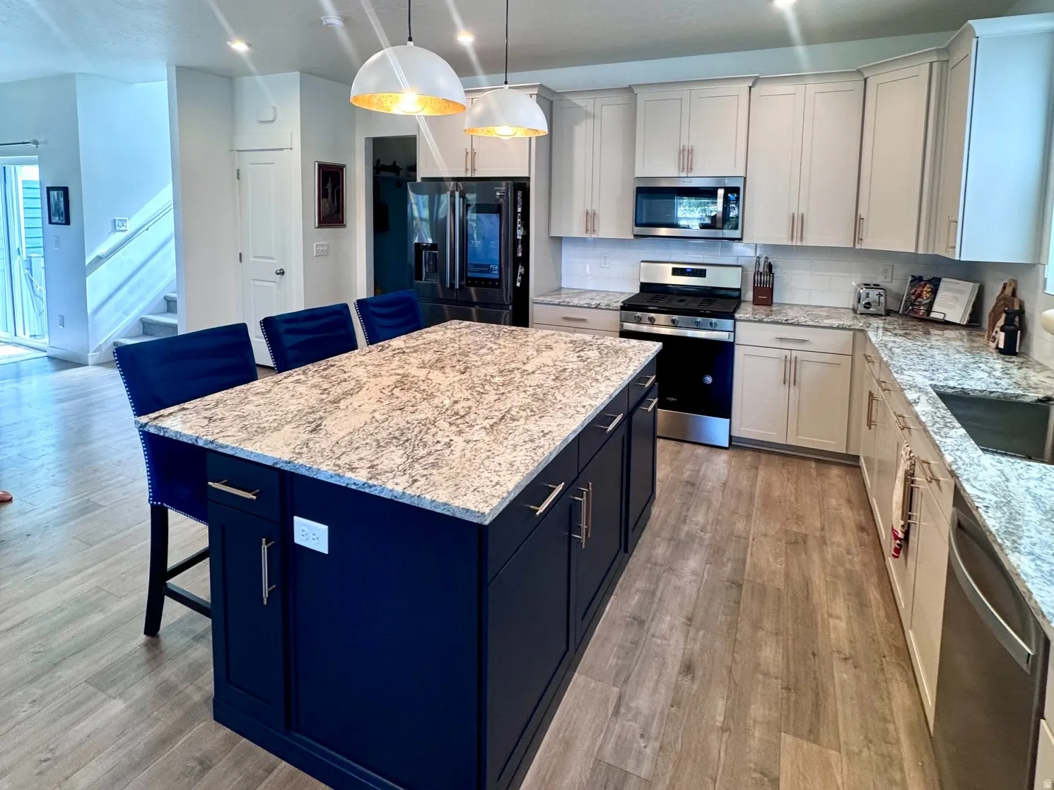 Spacious kitchen featuring a large central island with a light-colored countertop, white upper and lower cabinetry, stainless steel appliances, and wood-finish flooring
