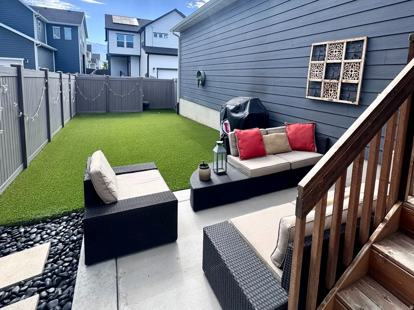 Expansive patio with stone stepping pads set in dark river rock, leading to an artificial turf lawn
