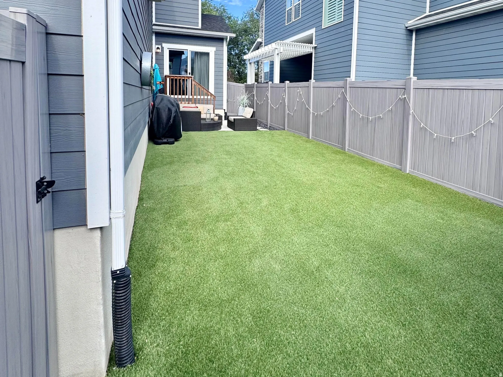 Fully fenced backyard featuring artificial turf, a wood deck with stairs, and a white pergola