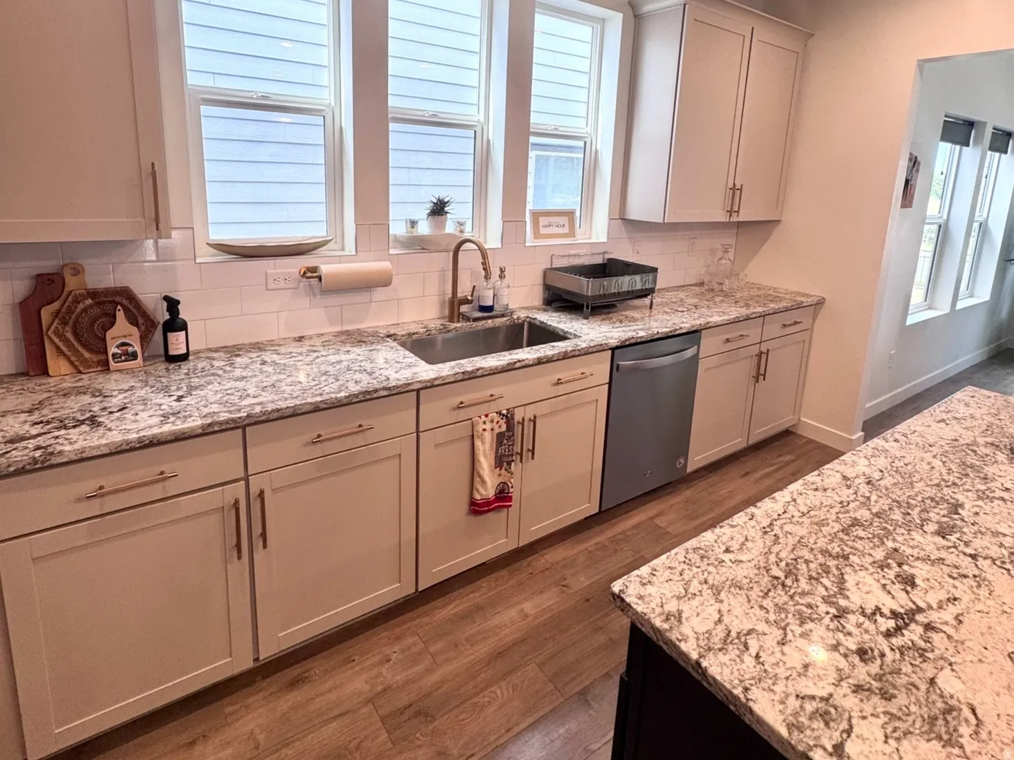 Kitchen featuring light-toned cabinetry, granite countertops, wood-finish flooring, a stainless steel sink, and a built-in dishwasher