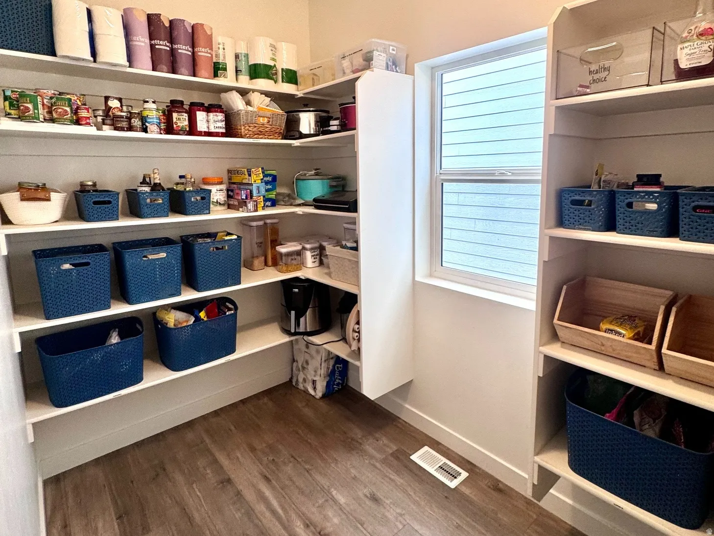 Spacious pantry featuring extensive built-in shelving, wood-finish flooring, and a window providing natural light