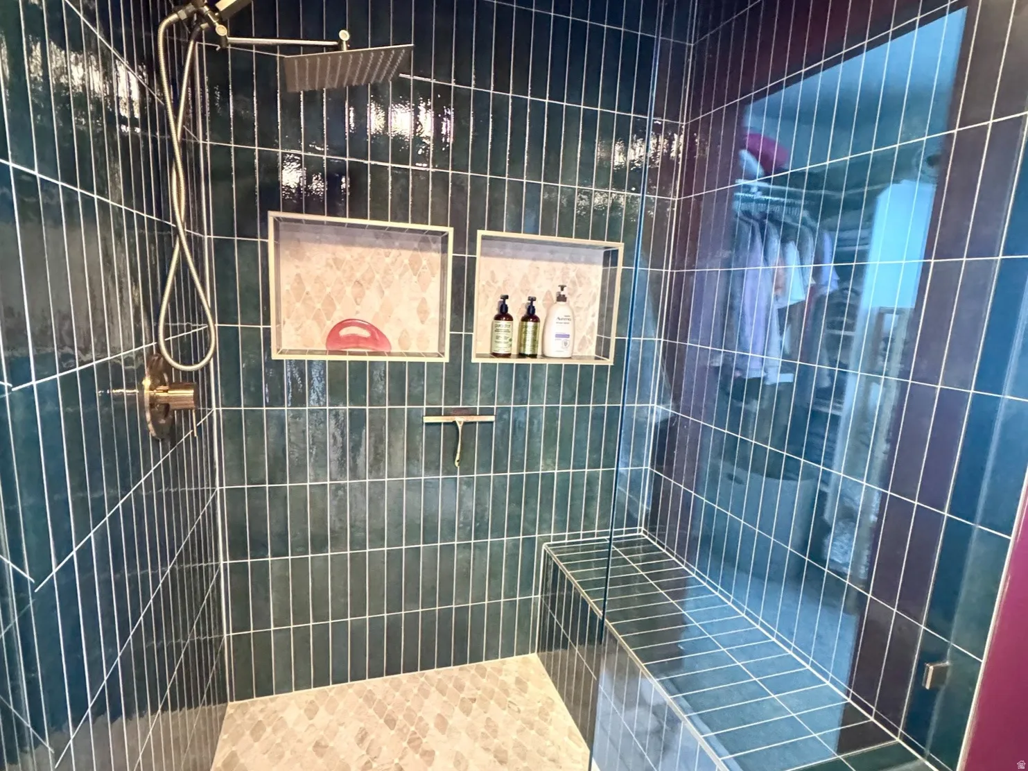 Custom-tiled shower featuring a rain showerhead, handheld sprayer, built-in bench, two recessed niches, and a glass enclosure