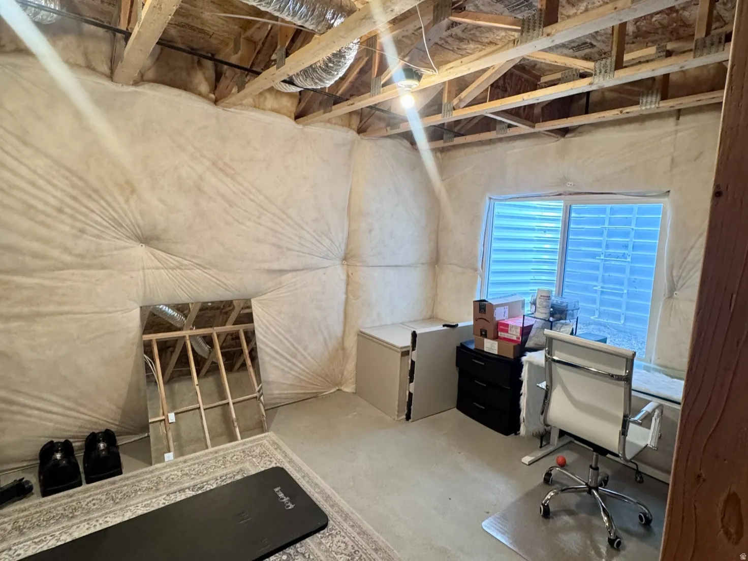 Unfinished basement space featuring exposed wood joists and ductwork, a window with horizontal blinds, and insulated walls