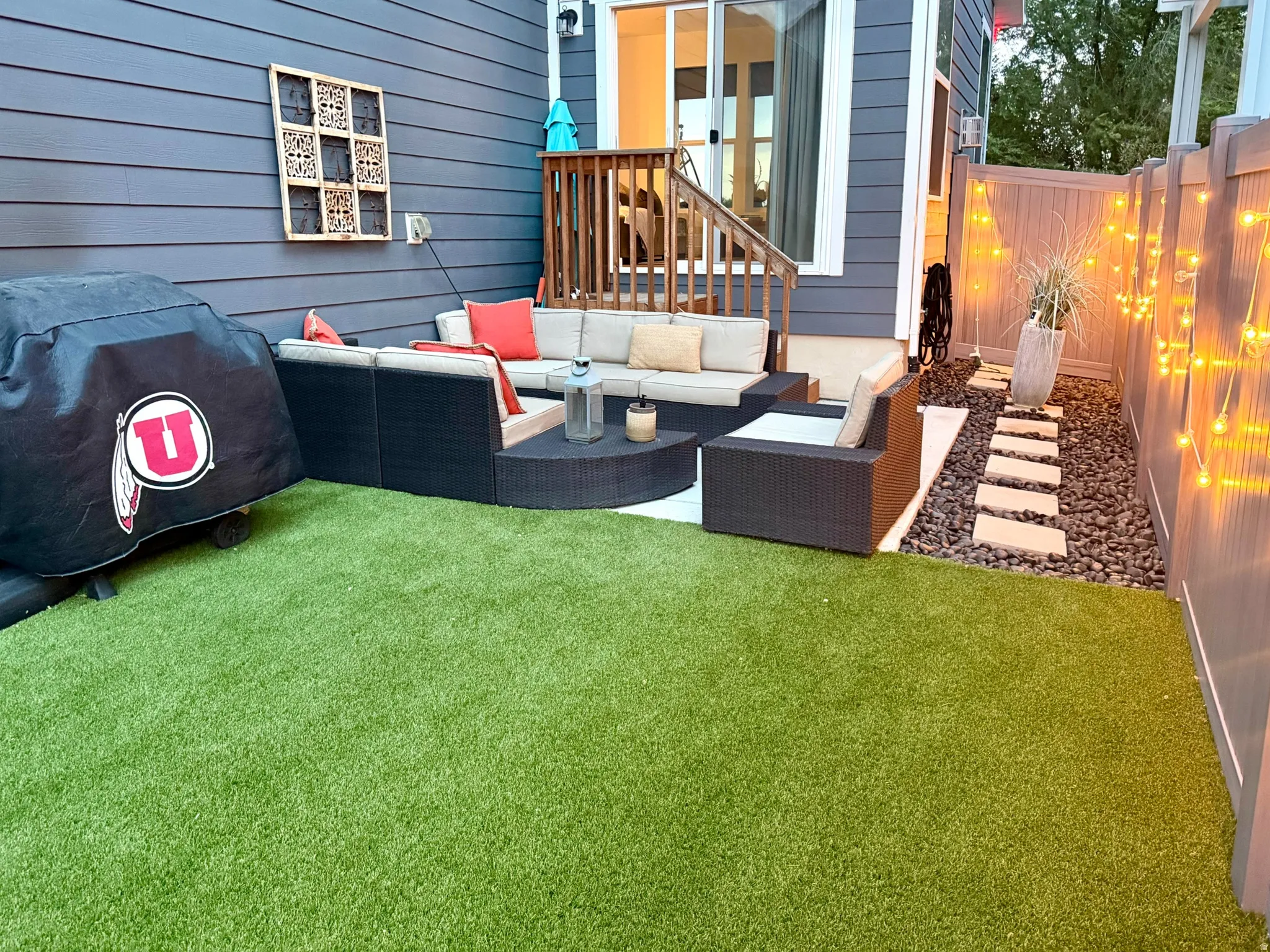 Fenced backyard featuring an artificial turf lawn, a patio area with built-in seating, a stone-stepped pathway, and a sliding glass door entry to the interior