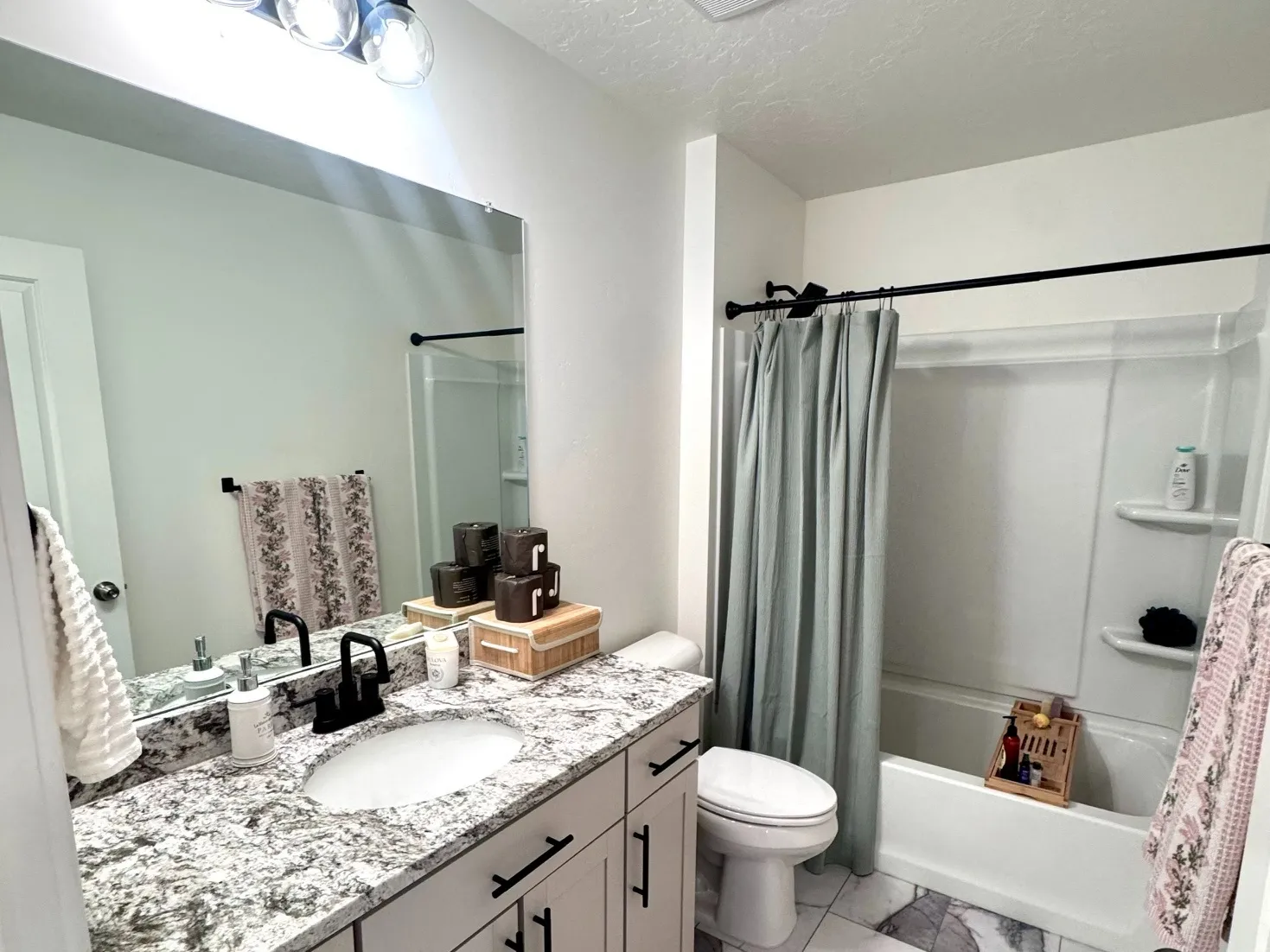 Bathroom featuring a single vanity with stone-look countertop, white cabinetry with matte black hardware, and an integrated basin