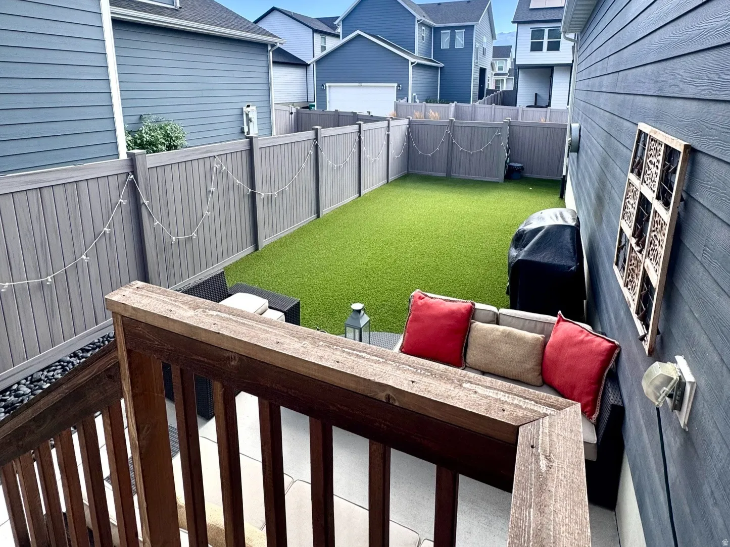 Private backyard featuring artificial turf, gray fencing, and a ground-level patio