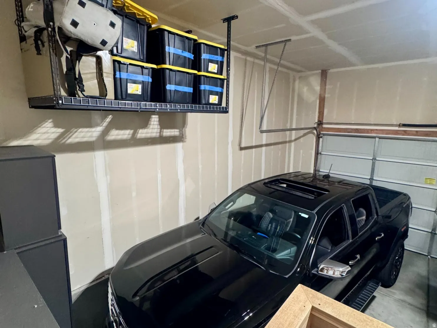 Garage interior featuring unfinished drywall, a ceiling-mounted storage rack, and a garage door with track system