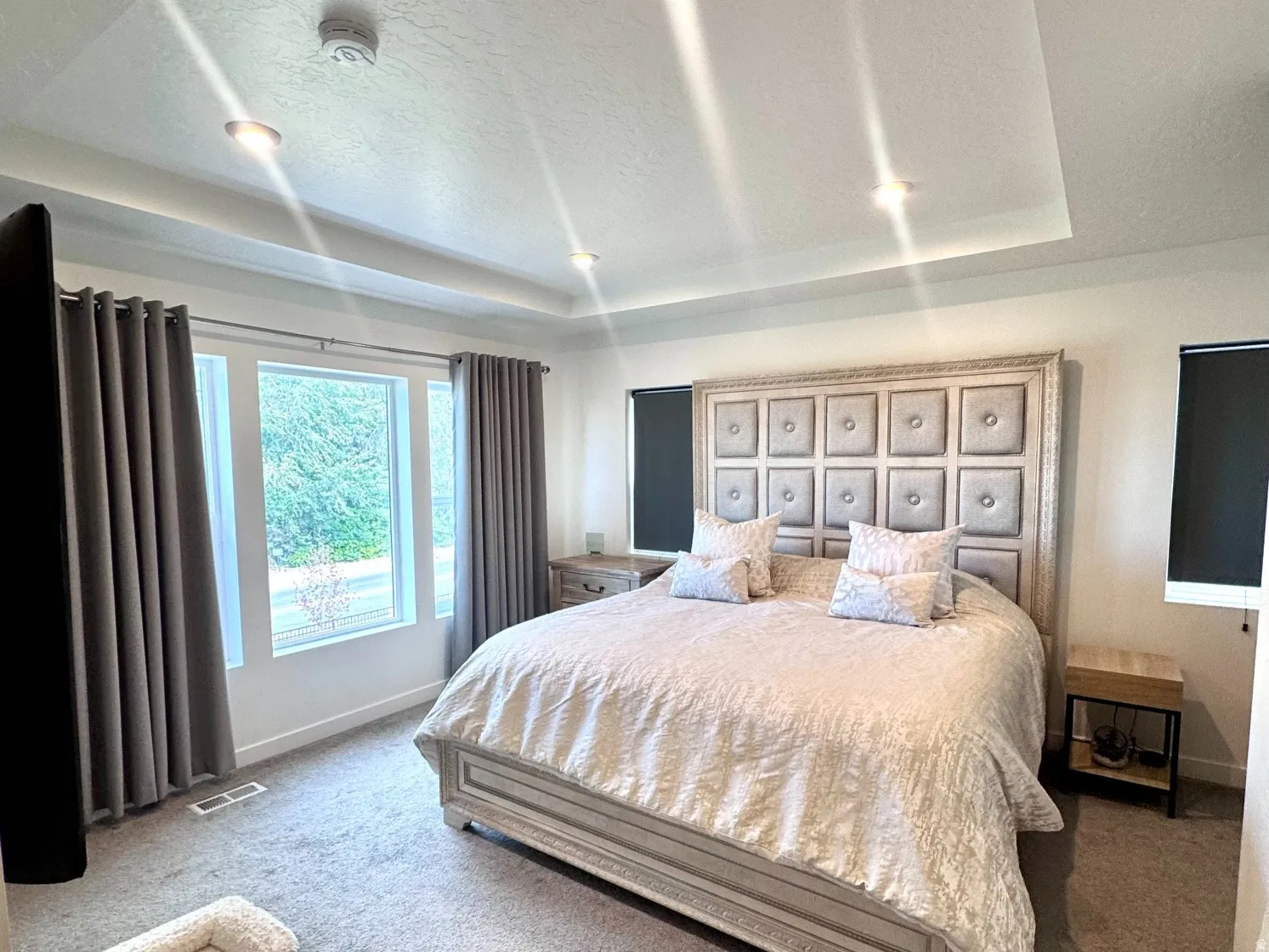 Recessed lighting illuminates a tray ceiling and plush gray carpeting