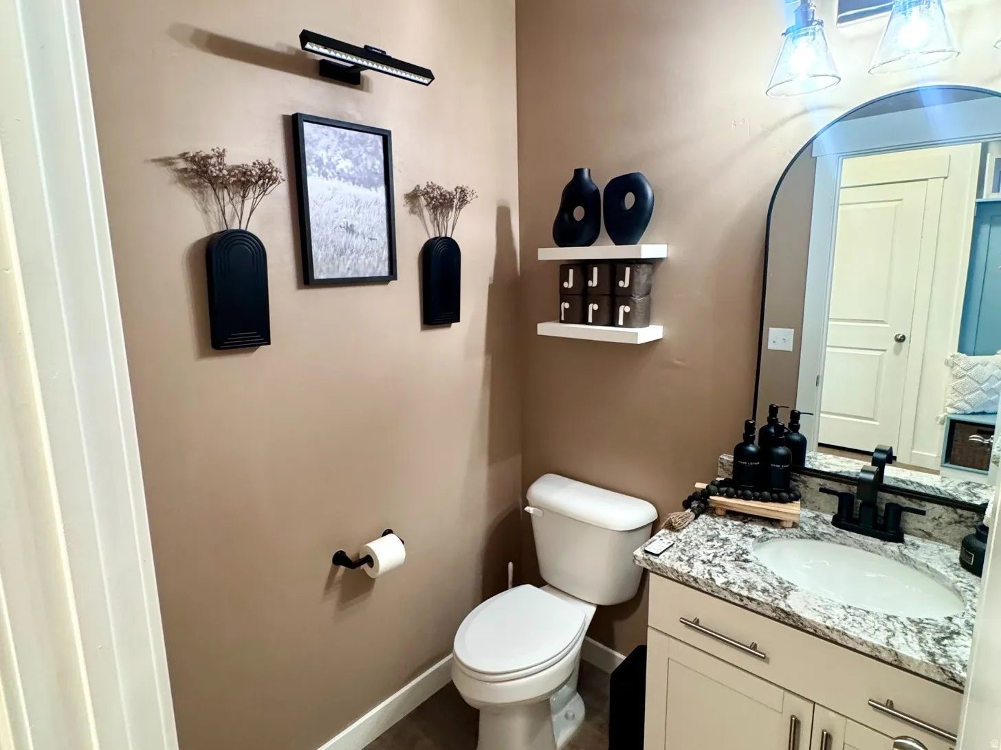 Powder room featuring wood-finish flooring, a contemporary vanity with a stone-finish countertop, and an arched mirror