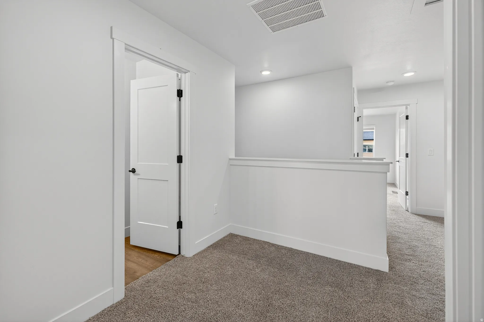 Carpeted hallway featuring white walls and trim, recessed lighting, and a partial wall with a cap rail