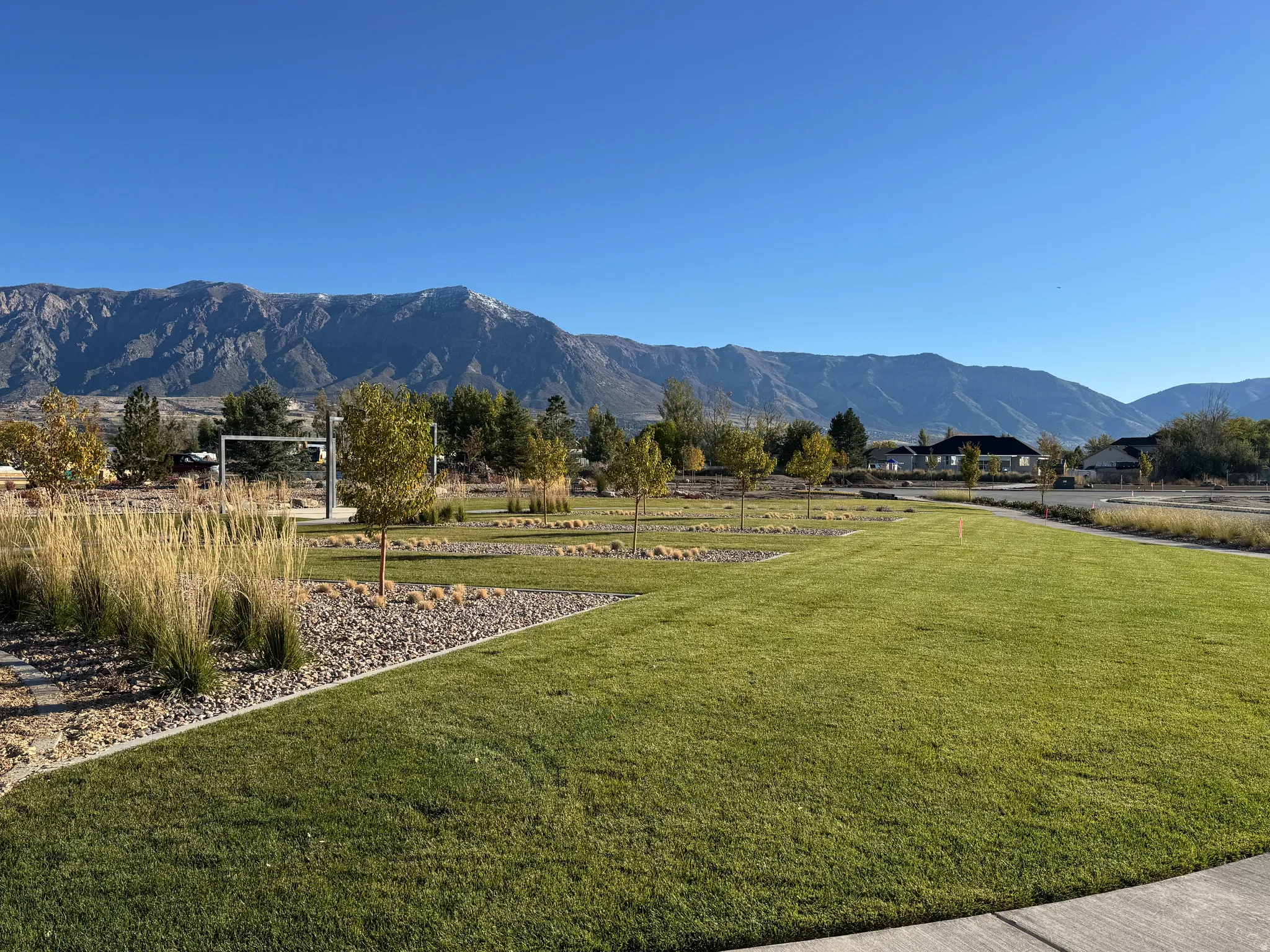 Expansive green space featuring manicured lawn, established landscaping, mountain backdrop, and a paved pathway