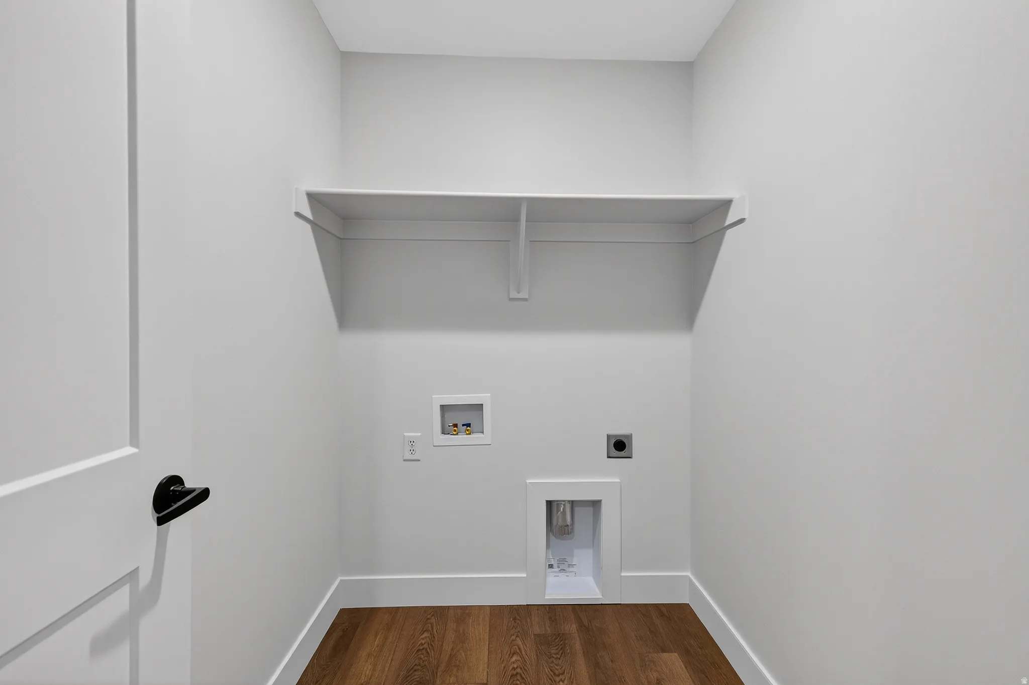 Dedicated utility space featuring a built-in shelf, wood-finish flooring, white baseboards, and essential hookups