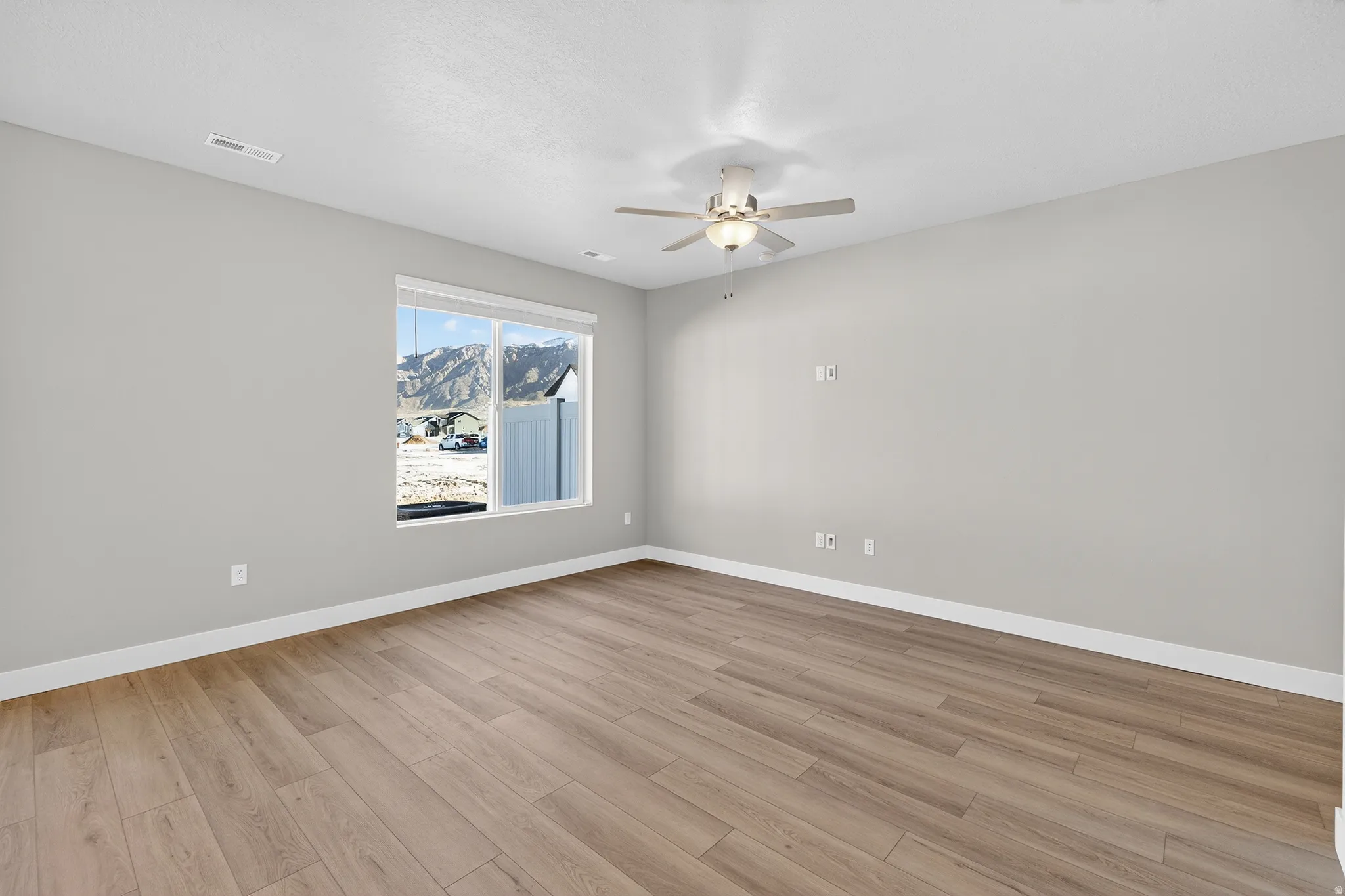 Spacious room with wood-finish flooring, light grey painted walls, and a multi-speed ceiling fan with integrated lighting