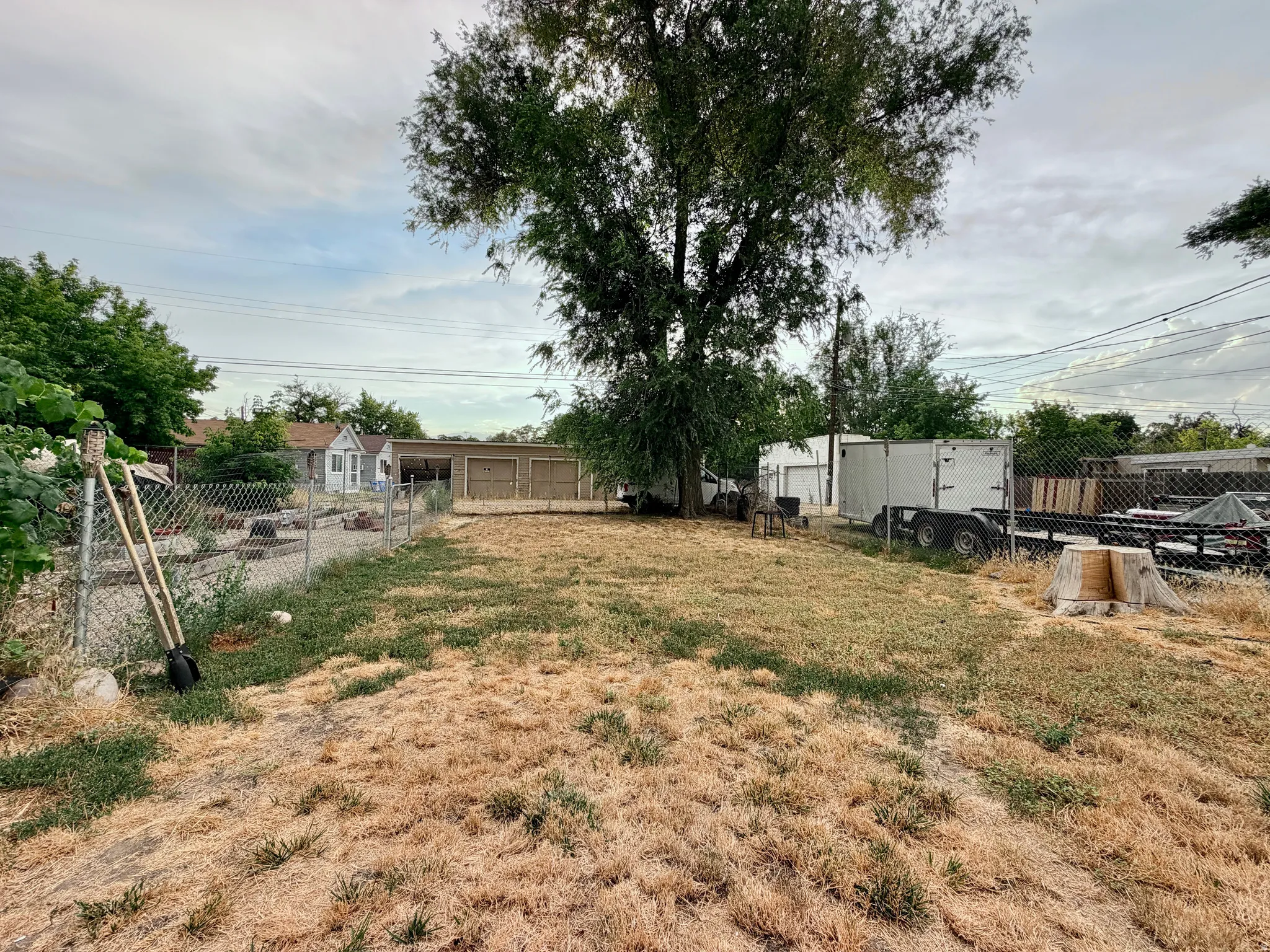Expansive grassy lot with mature trees, chain-link fencing.