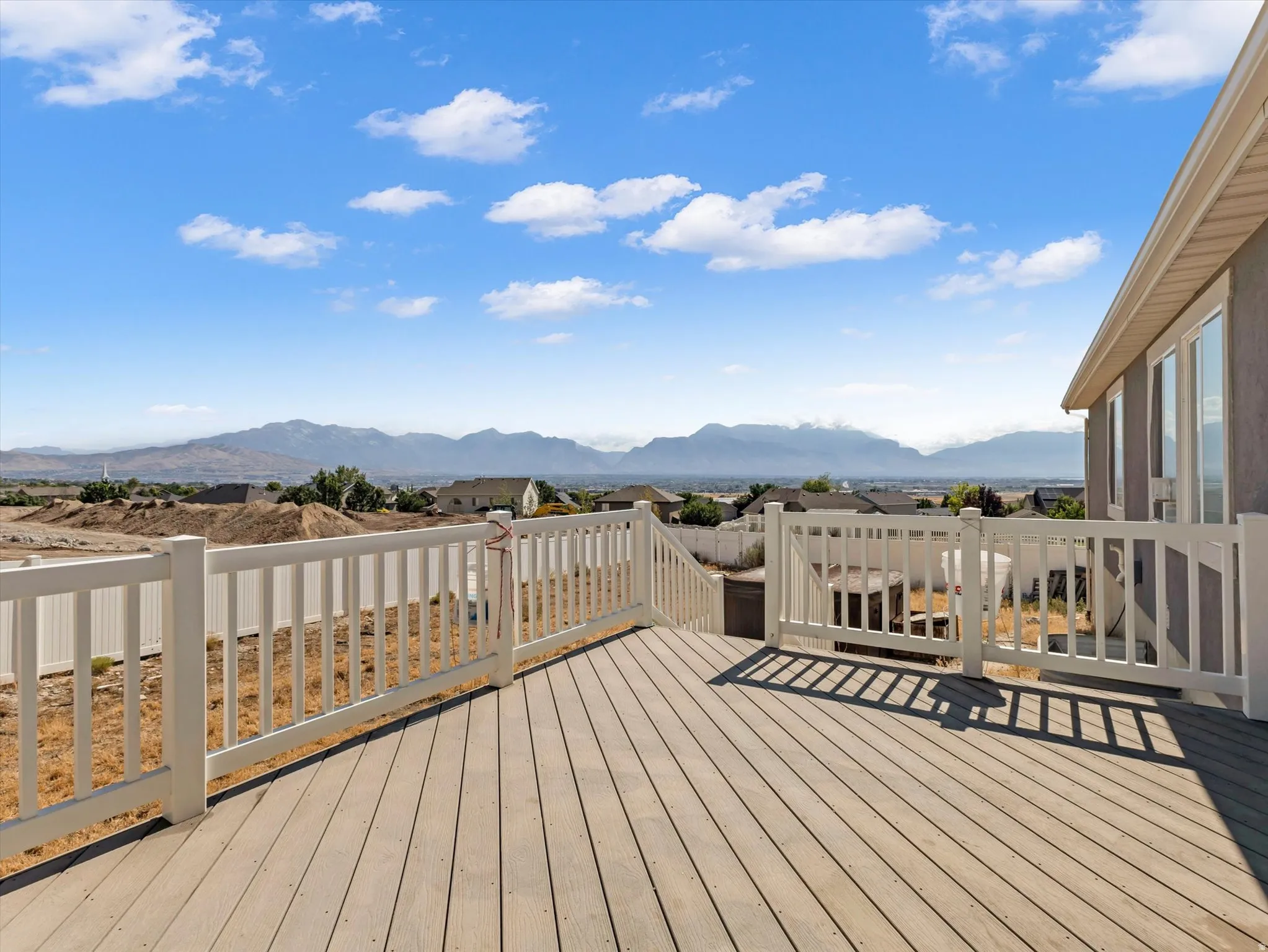 Expansive wood-finish deck with white railings and staircase, offering broad mountain scenery