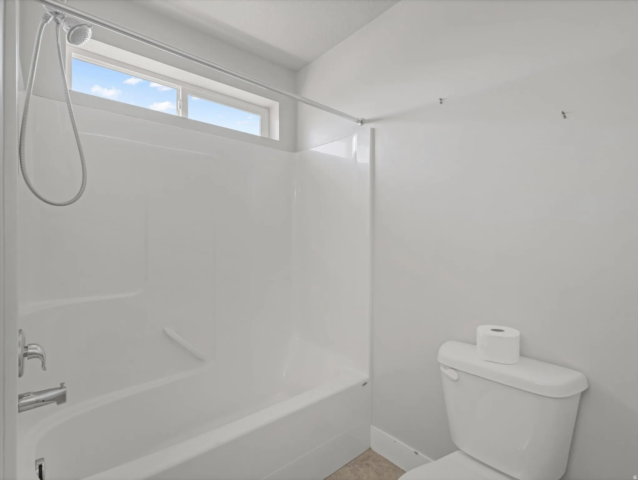 Bathroom featuring a white tub/shower combination with chrome fixtures and a high transom window