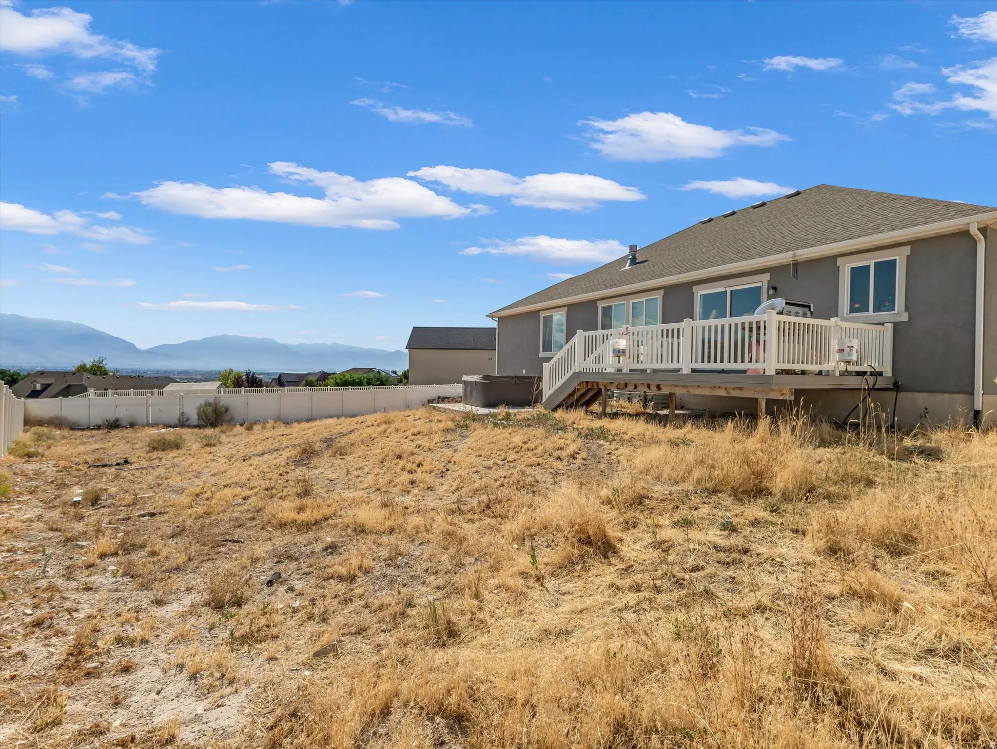 Rear exterior featuring a spacious elevated deck with white railings, multiple sliding glass doors, and a neutral stucco finish