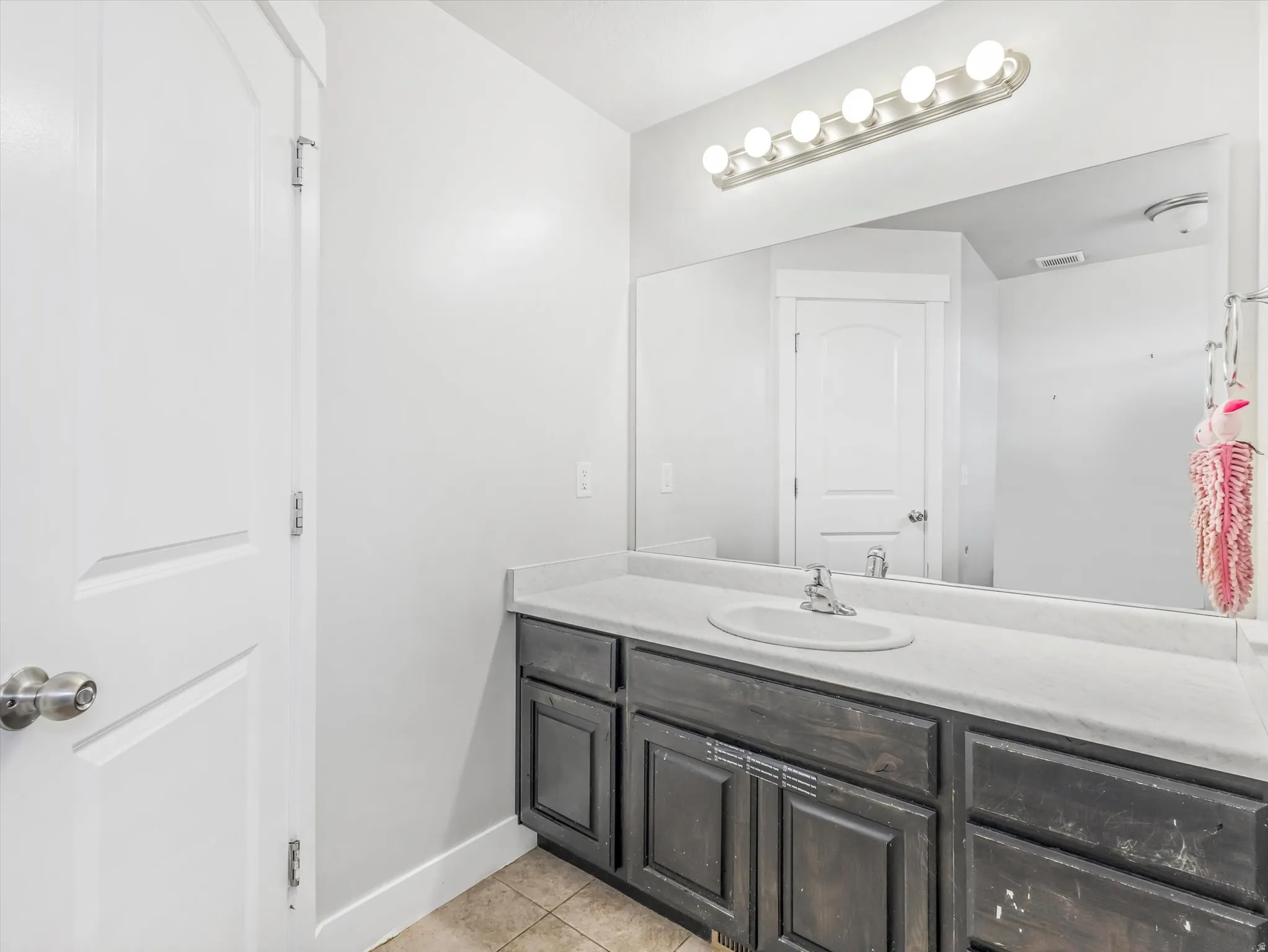 Bathroom vanity featuring a single basin sink set in a light-toned countertop, with a dark wood-finish cabinet below