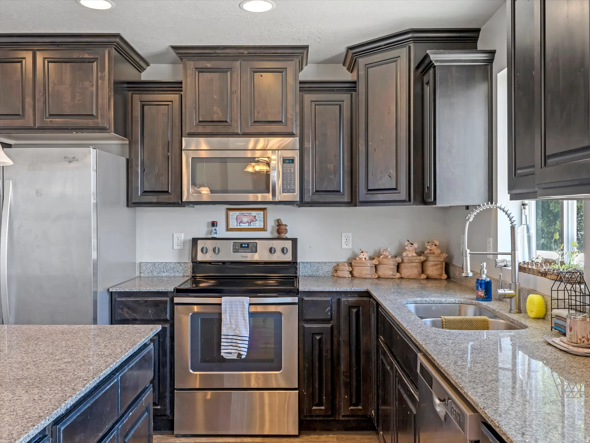 Kitchen featuring dark wood cabinetry with crown molding, light-toned countertops, and stainless steel appliances including a refrigerator, range, microwave, and dishwasher