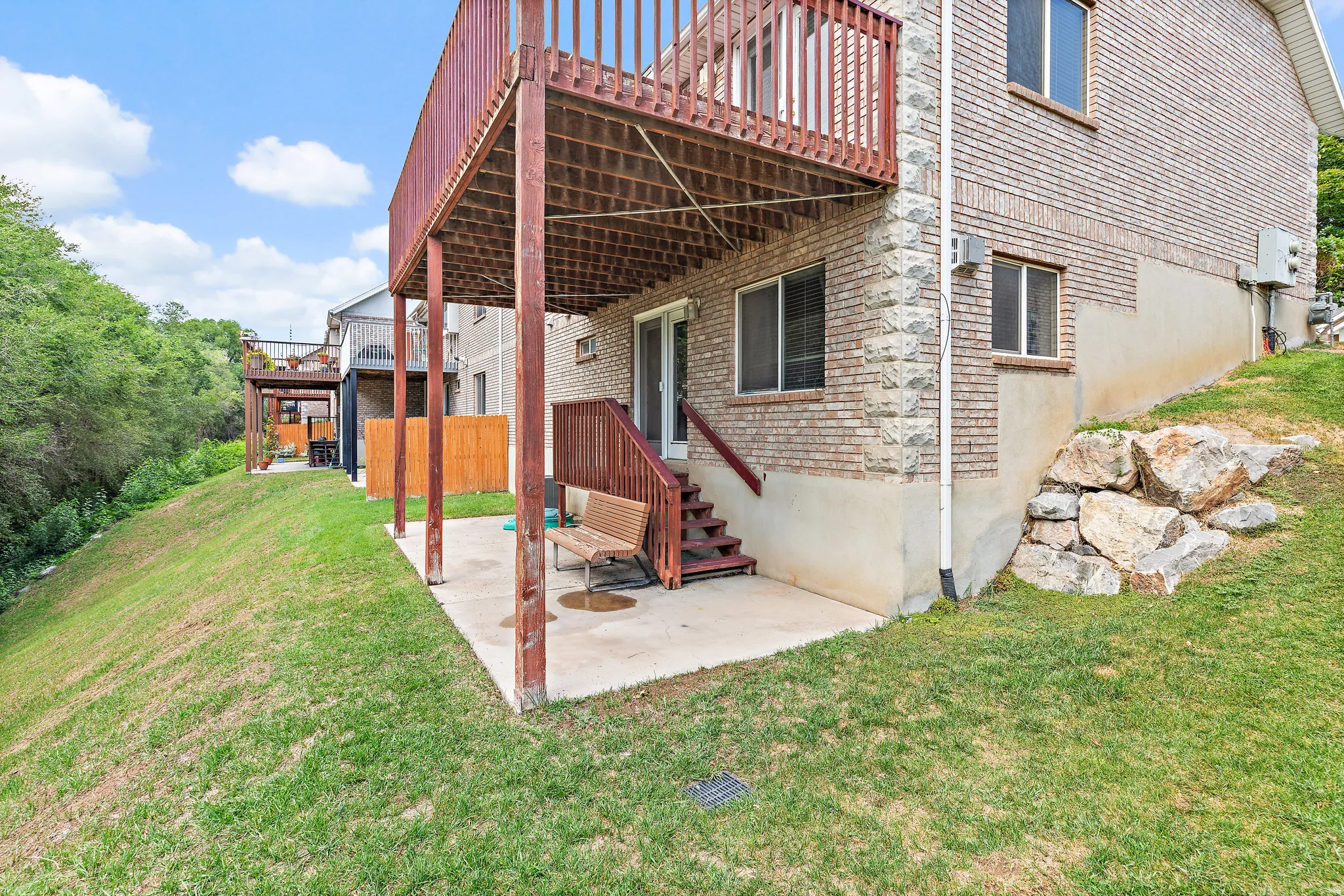 Rear exterior featuring a ground-level patio, a red wood-tone deck, and a sloped lawn