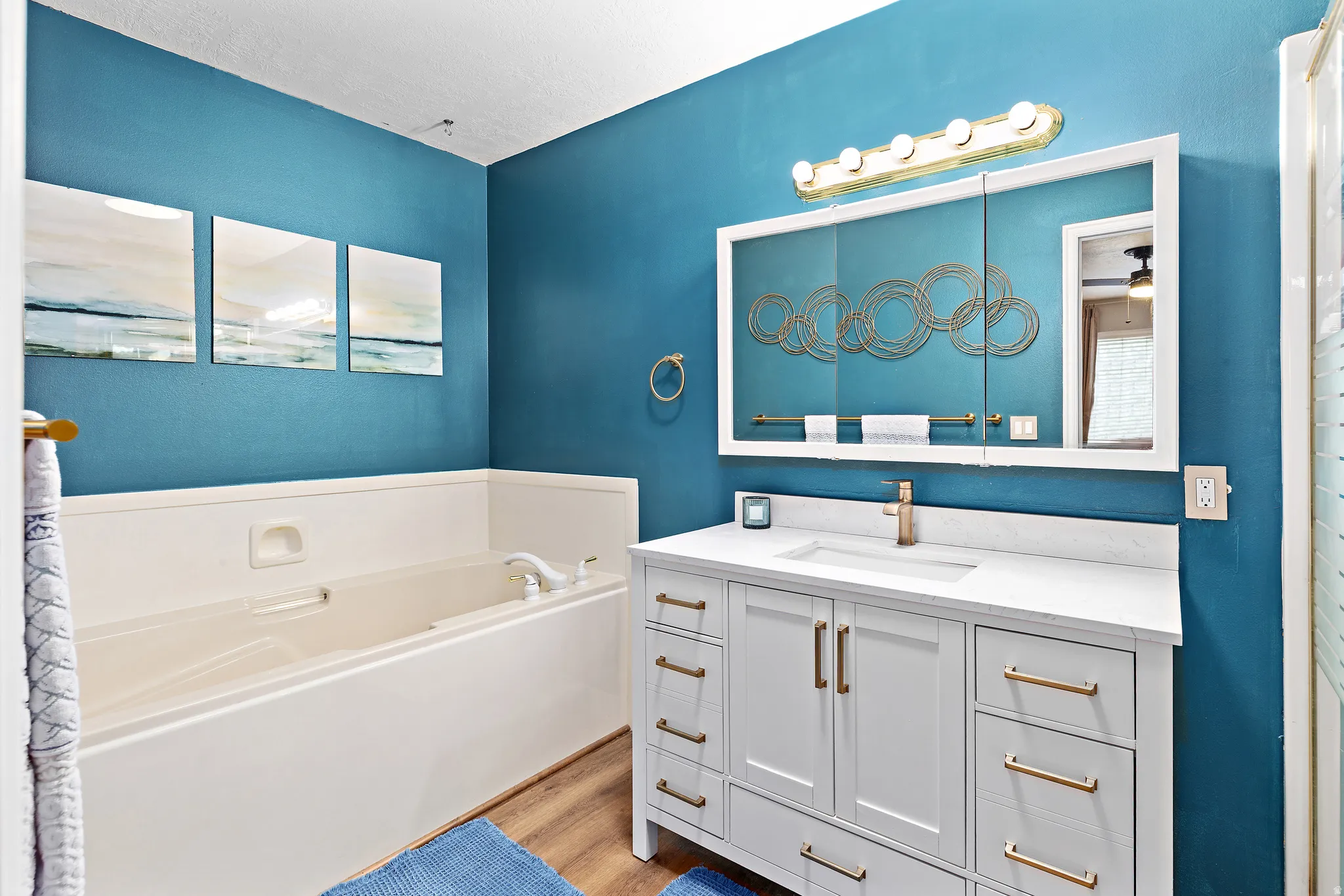 Bathroom featuring a built-in tub, a single vanity with a white countertop, a rectangular undermount sink, and wood-finish flooring