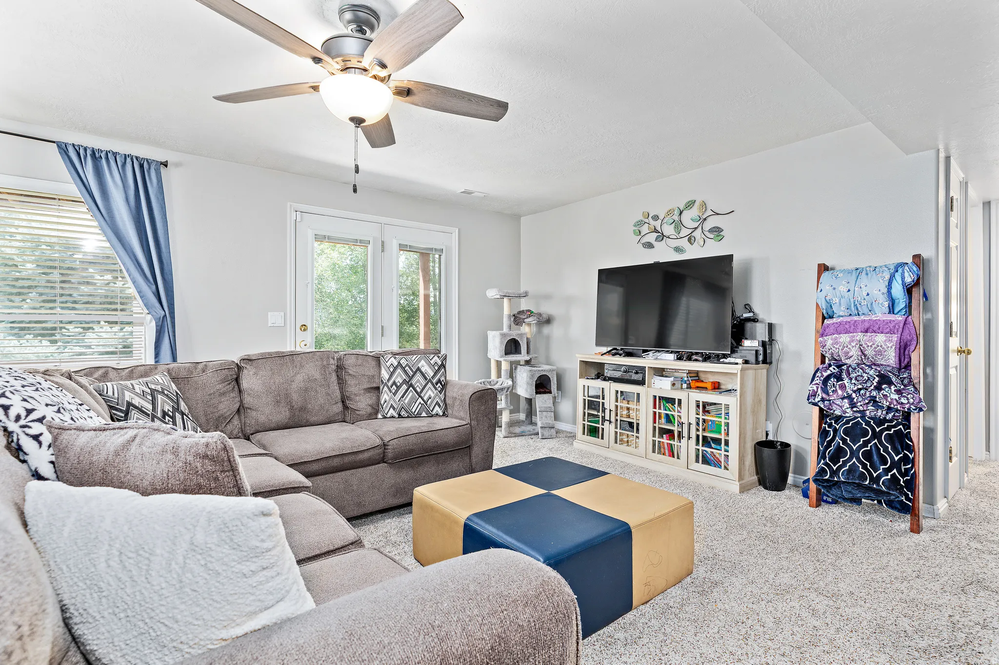 Carpeted living space featuring a ceiling fan with integrated lighting, glass French doors, and a window with blinds