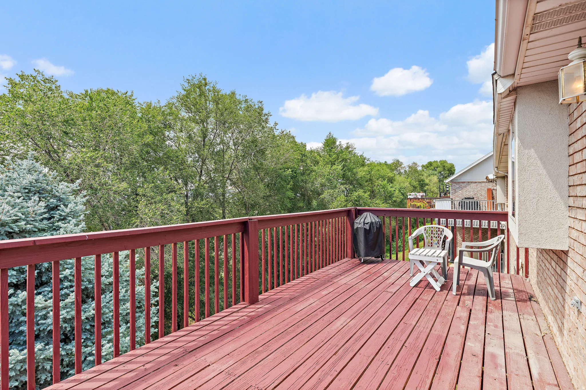 Spacious outdoor deck with deep red wood finish, surrounded by mature trees