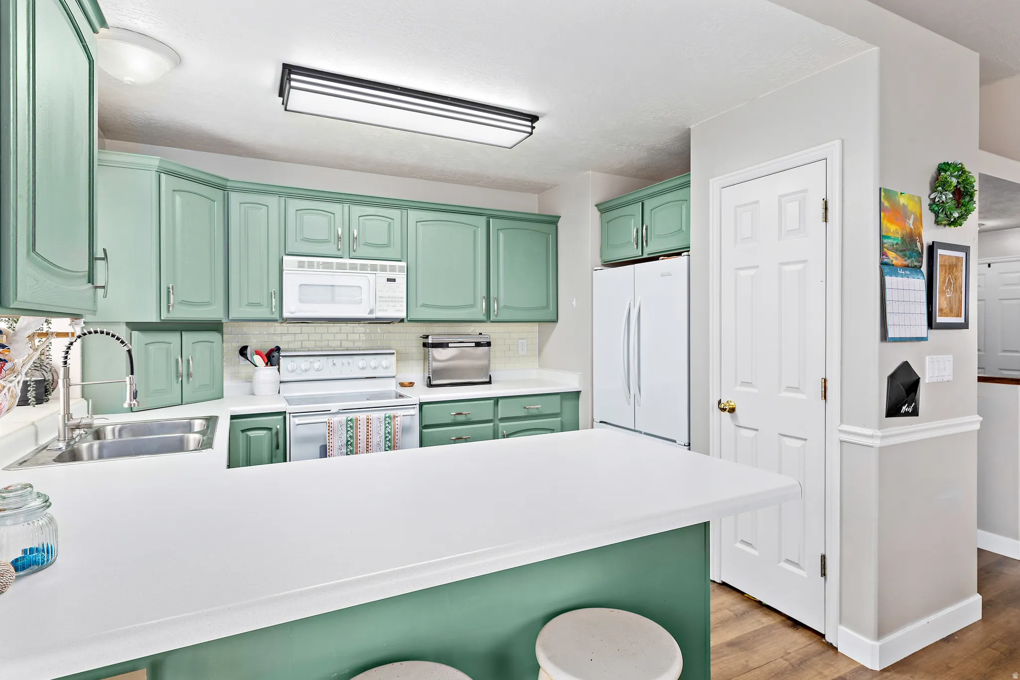 Kitchen featuring a white countertop island, mint green cabinetry, a double basin stainless steel sink with a high-arc faucet, and white appliances including an oven range, microwave, and refrigerator