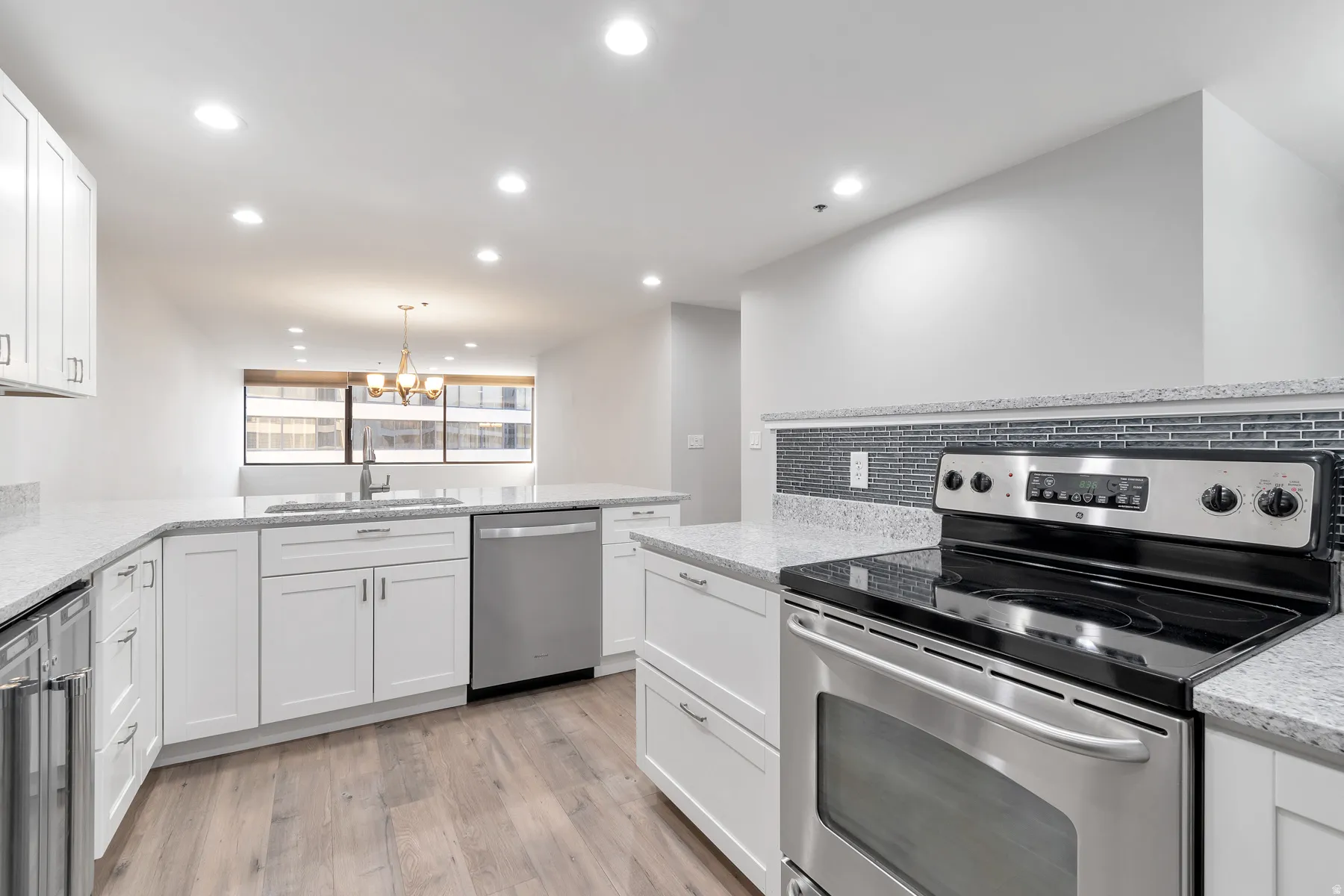 Spacious kitchen featuring white cabinetry, granite countertops, a glass tile backsplash, stainless steel appliances, and laminate flooring
