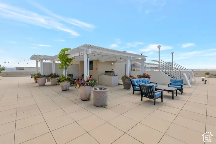 Expansive rooftop patio featuring large format tile flooring, a white pergola structure, built-in outdoor kitchen area, and string lighting