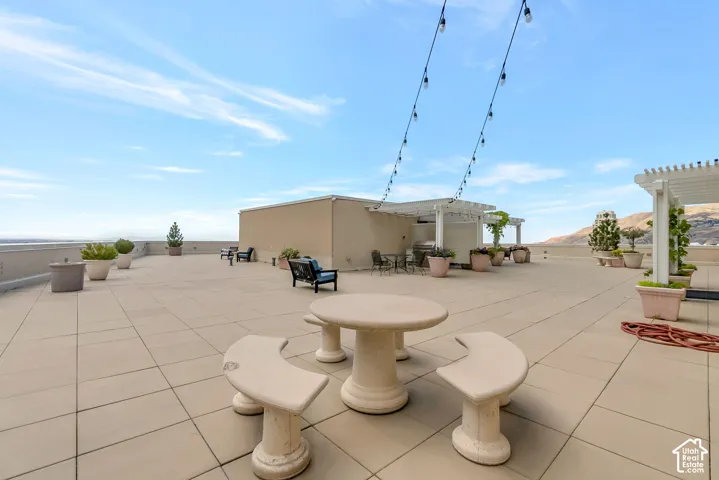 Expansive rooftop patio featuring large format tile flooring, string lighting, and multiple pergolas providing shaded areas