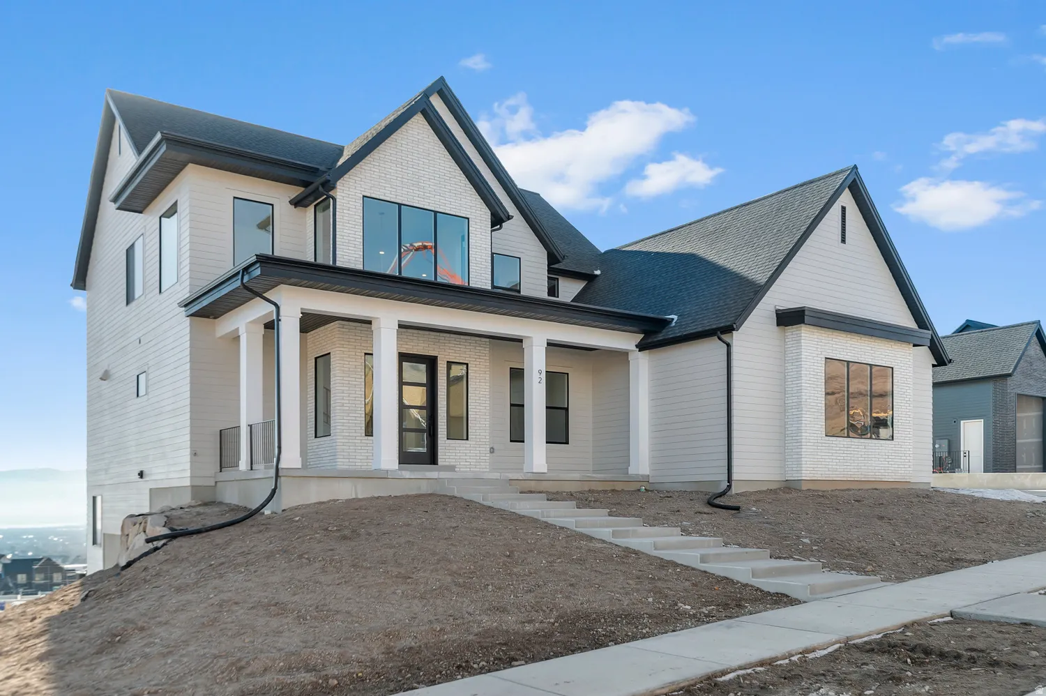 Contemporary residence featuring a light-toned brick facade, vertical siding accents, a prominent covered entry with white columns, black-framed windows, and a black shingle roof