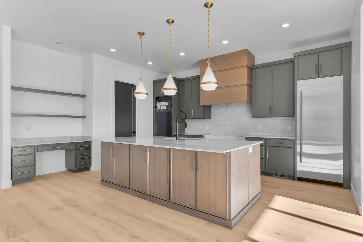 Expansive kitchen featuring a large central island with a white countertop, light wood-finish cabinetry, and three pendant lights