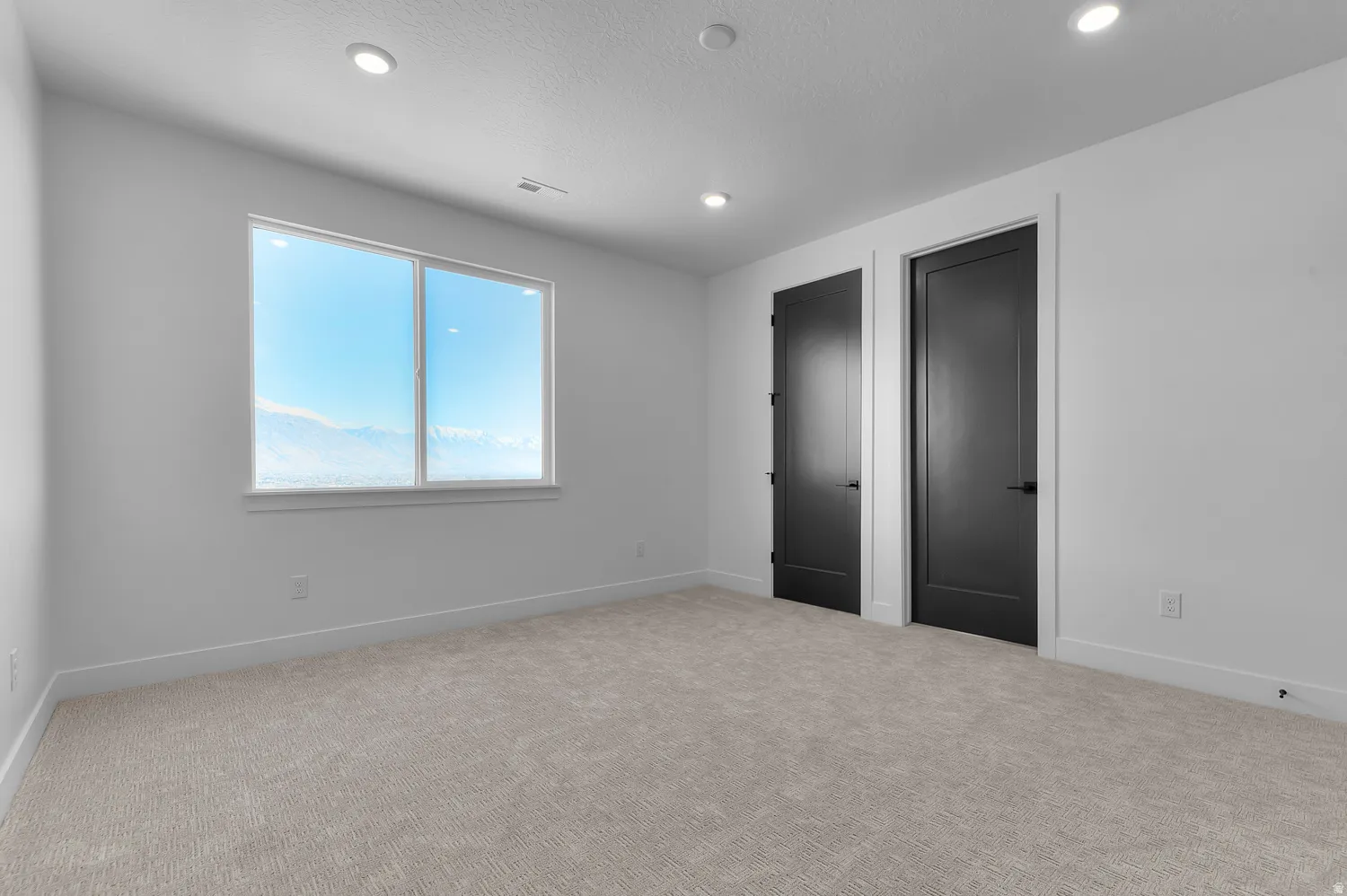 Bright room featuring a large window, recessed lighting, neutral carpet, and two modern black doors